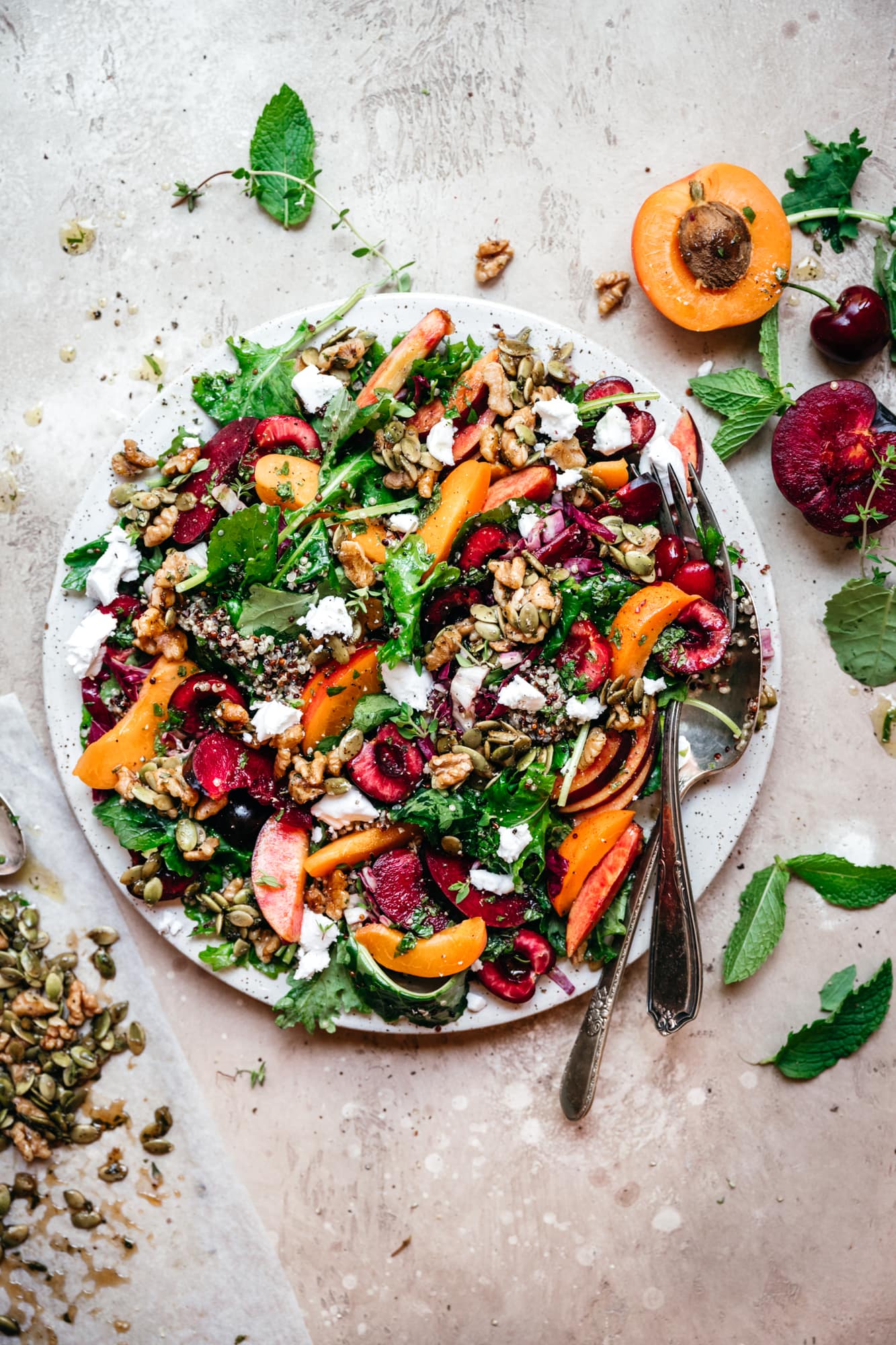 overhead view of kale and stone fruit salad with quinoa and feta on white plate