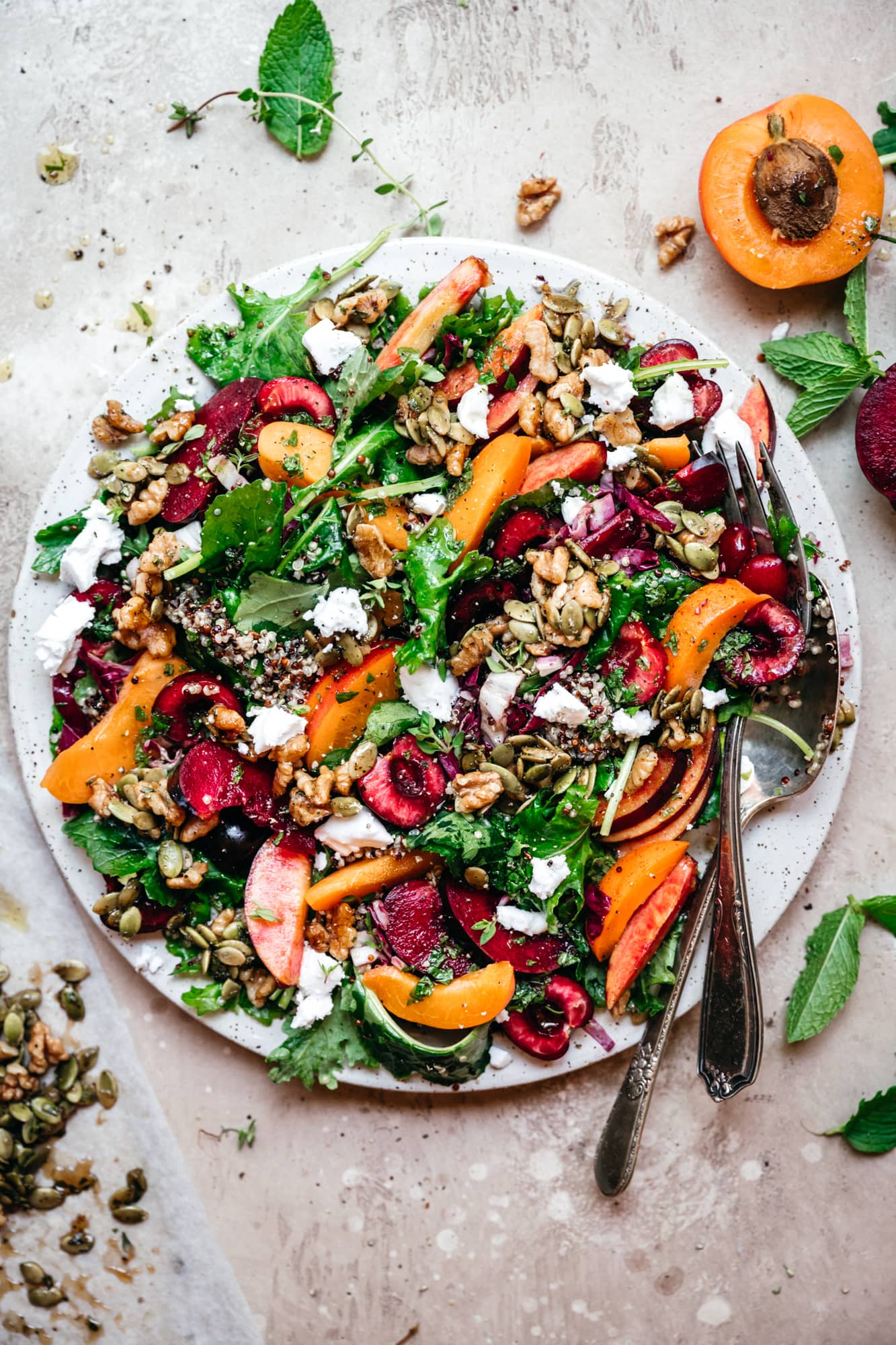 overhead view of kale and stone fruit salad with quinoa and feta on white plate