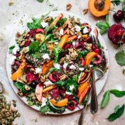 overhead view of kale and stone fruit salad with quinoa and feta on white plate