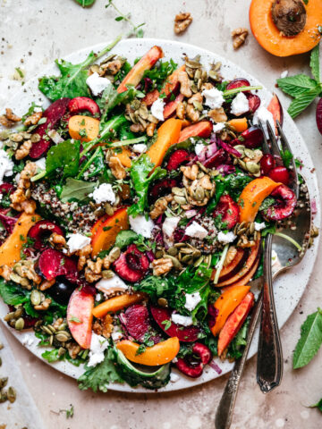 overhead view of kale and stone fruit salad with quinoa and feta on white plate