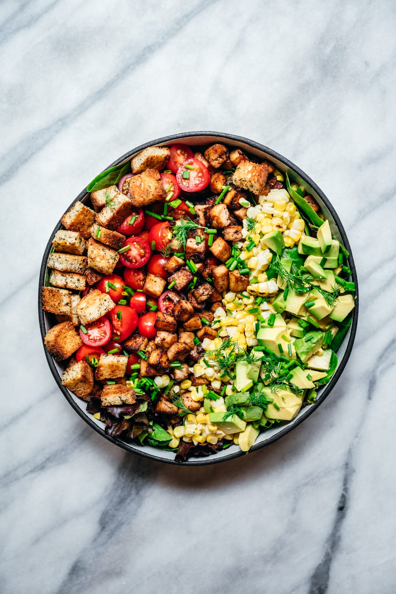 overhead view of vegan avocado BLT salad on marble backdrop