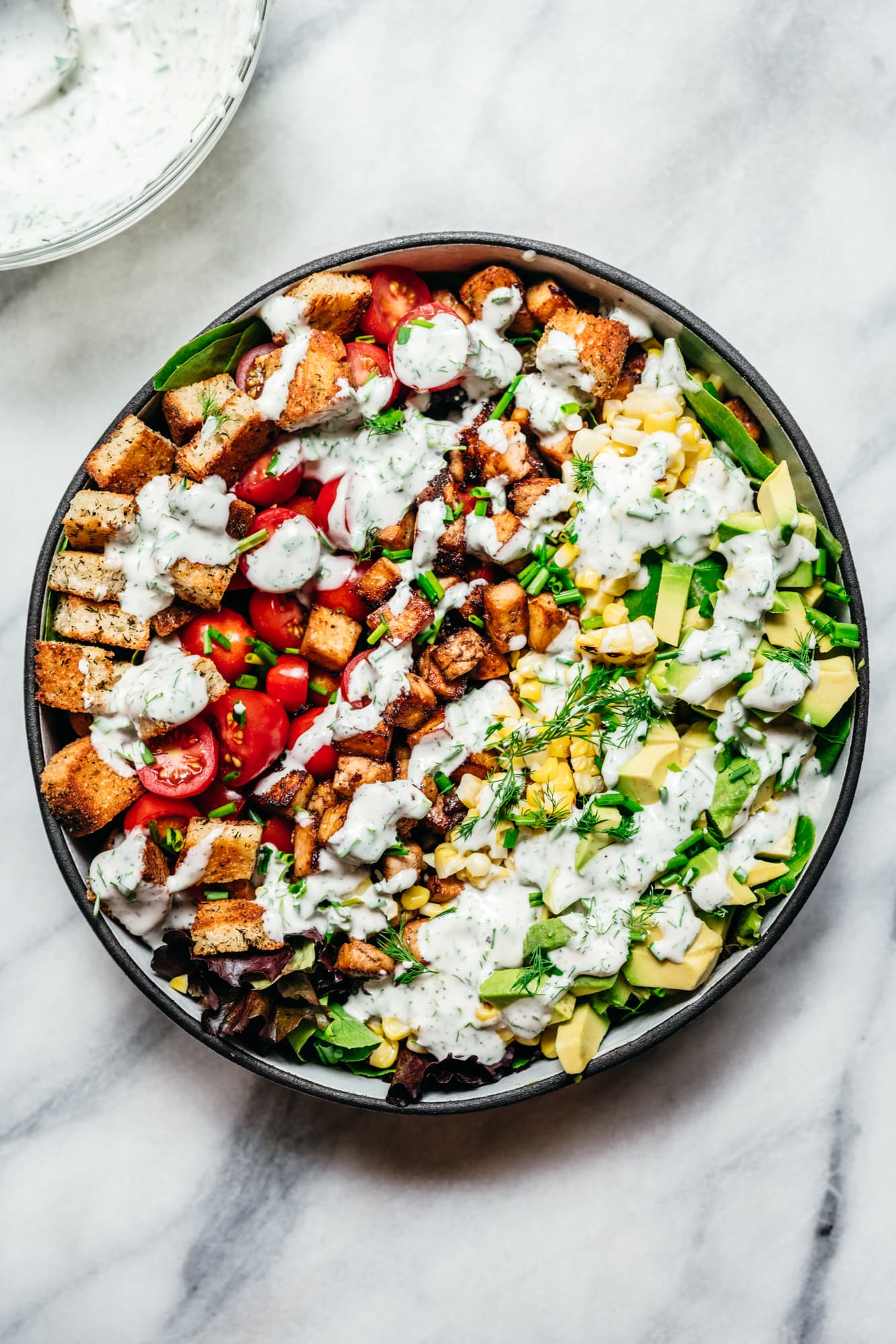 overhead view of vegan avocado BLT salad with ranch dressing on marble backdrop