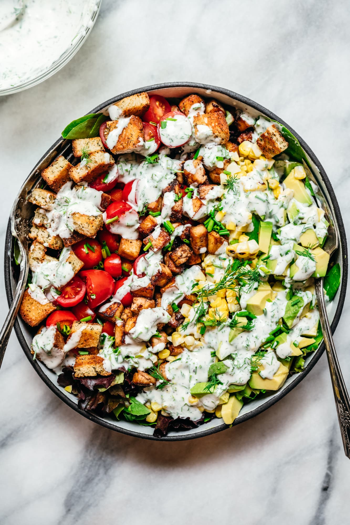 overhead view of vegan avocado BLT salad with ranch dressing on marble backdrop