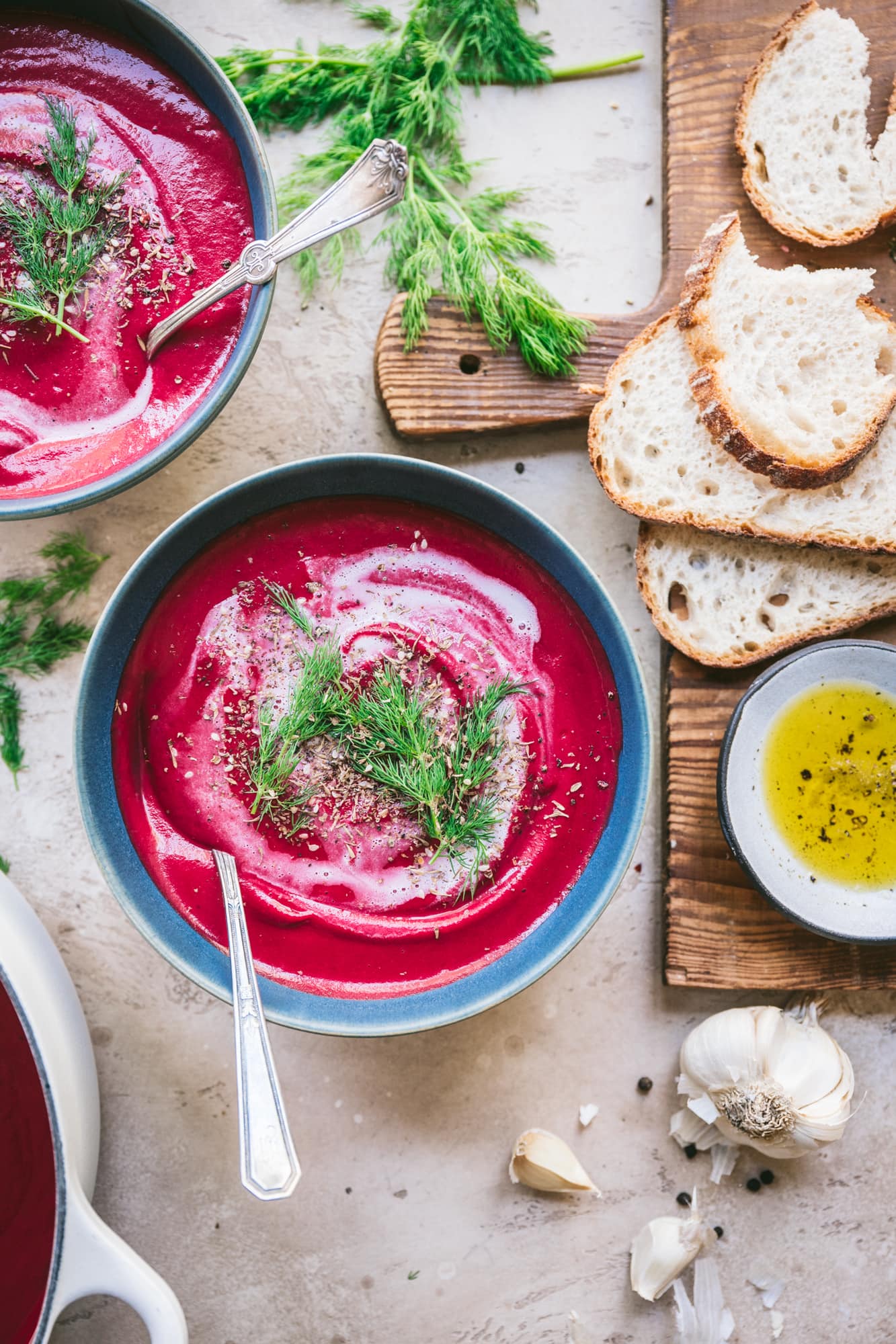 overhead view of vegan roasted beet soup with yogurt swirl and dill with bread for serving