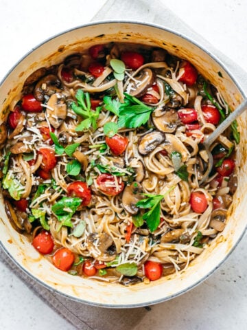 overhead view of vegan one pot pasta in a dutch oven with mushrooms and tomatoes.