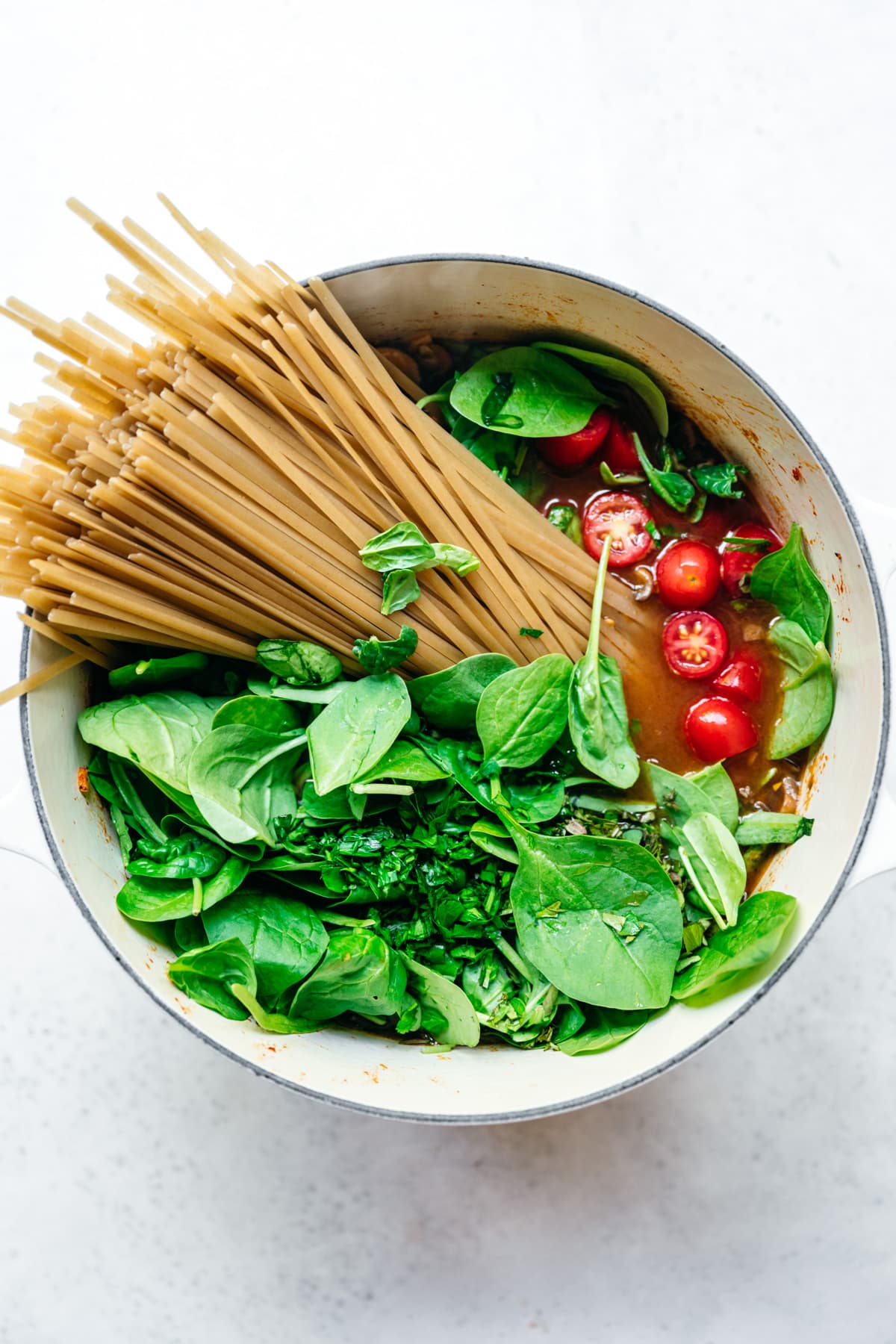 overhead view of ingredients for one pot pasta with spinach and tomatoes in a white dutch oven.