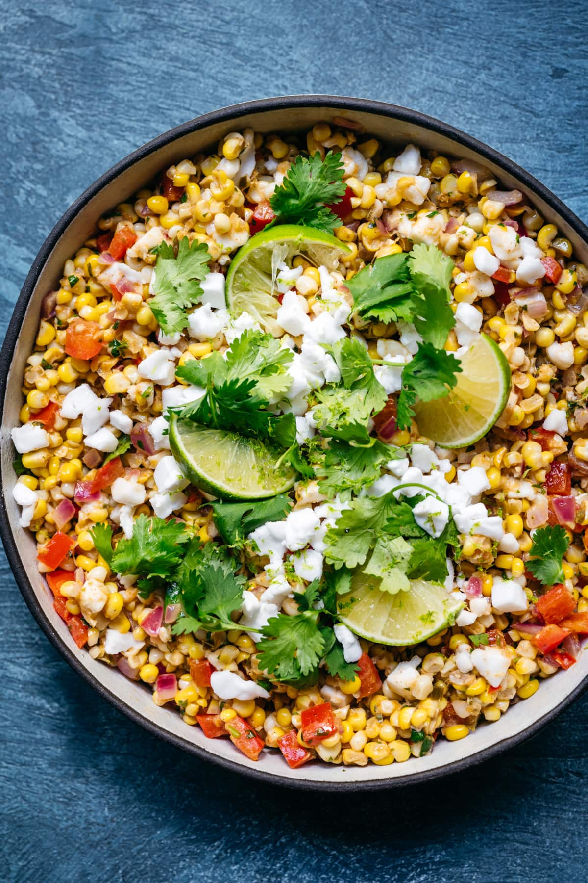 overhead view of bowl of vegan mexican street corn salad with limes and cilantro