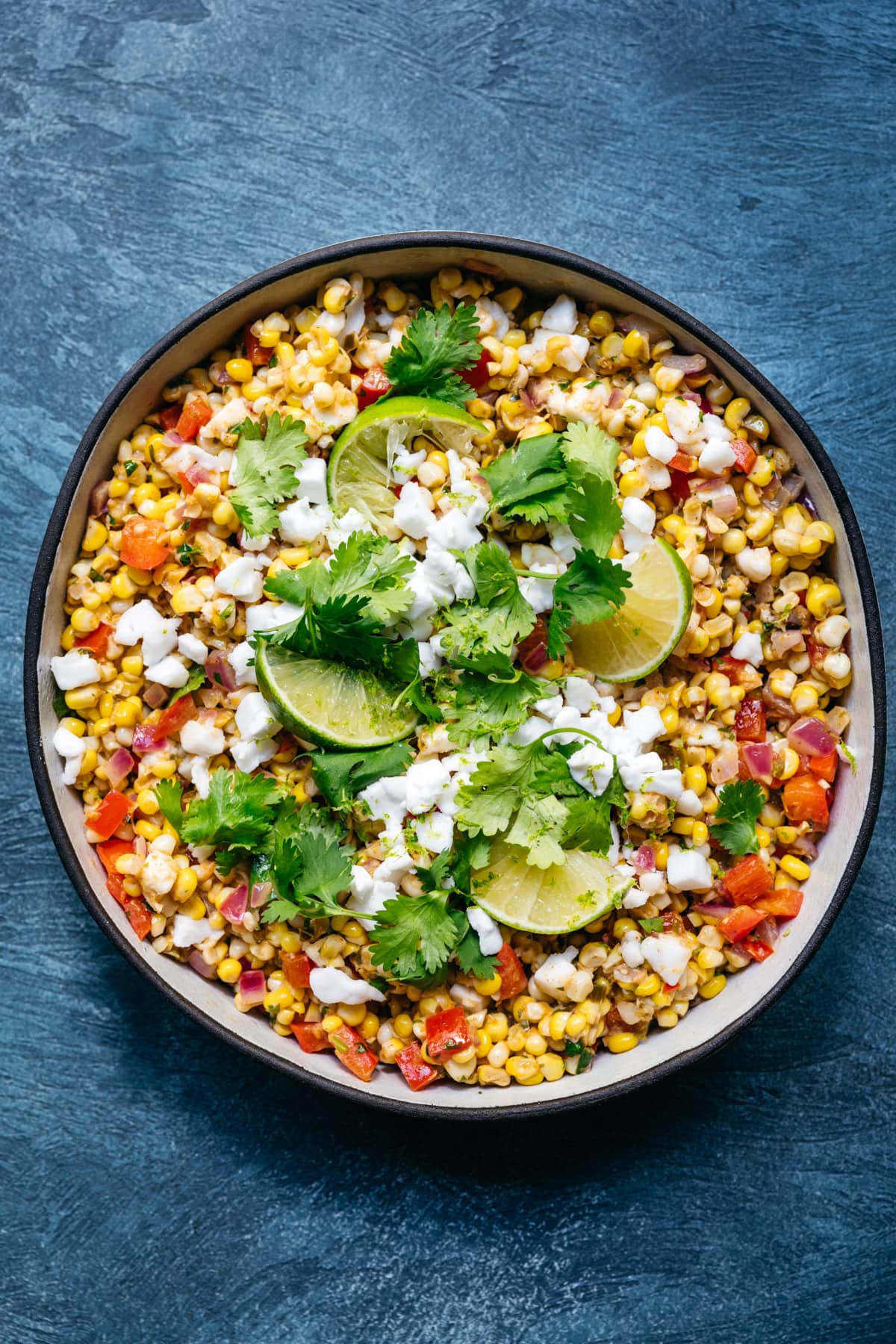 overhead view of bowl of vegan mexican street corn salad with limes and cilantro