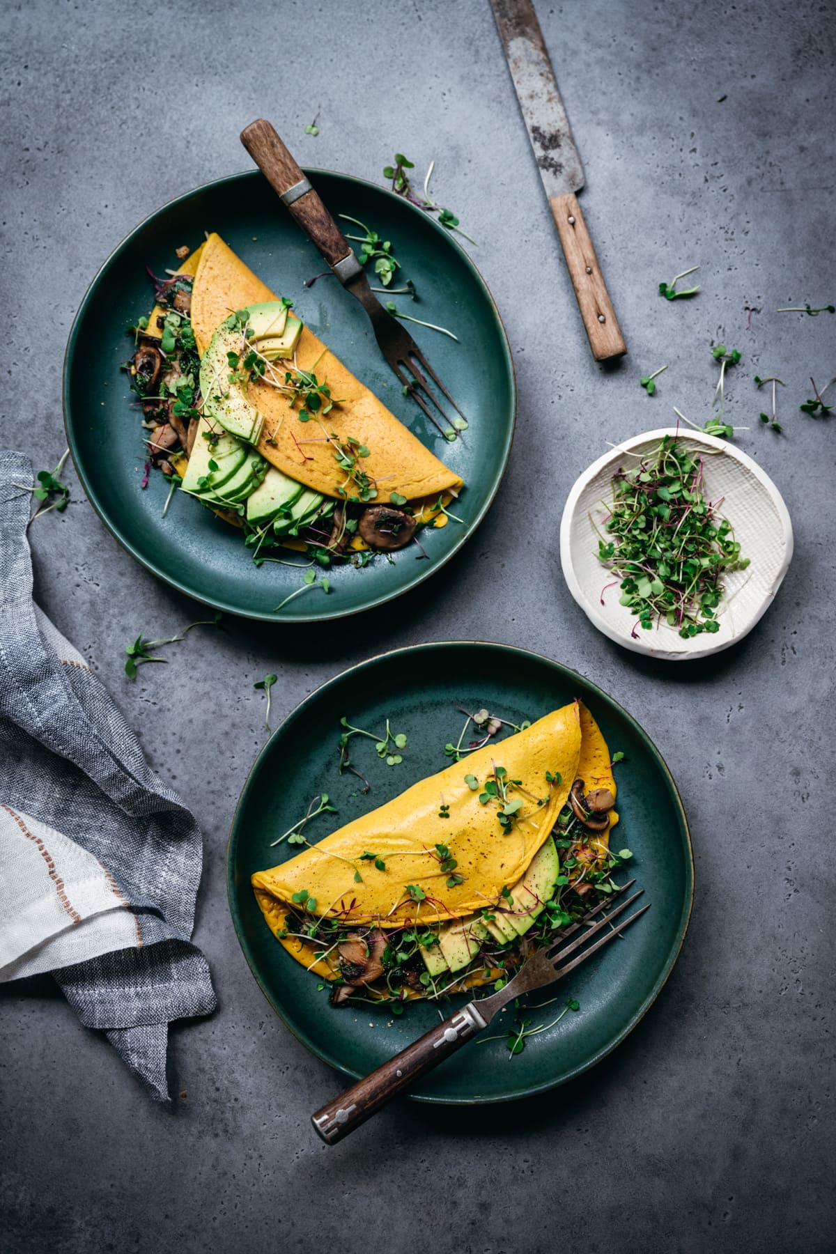 overhead view of two plates of vegan omelettes with mushrooms, spinach and avocado filling.