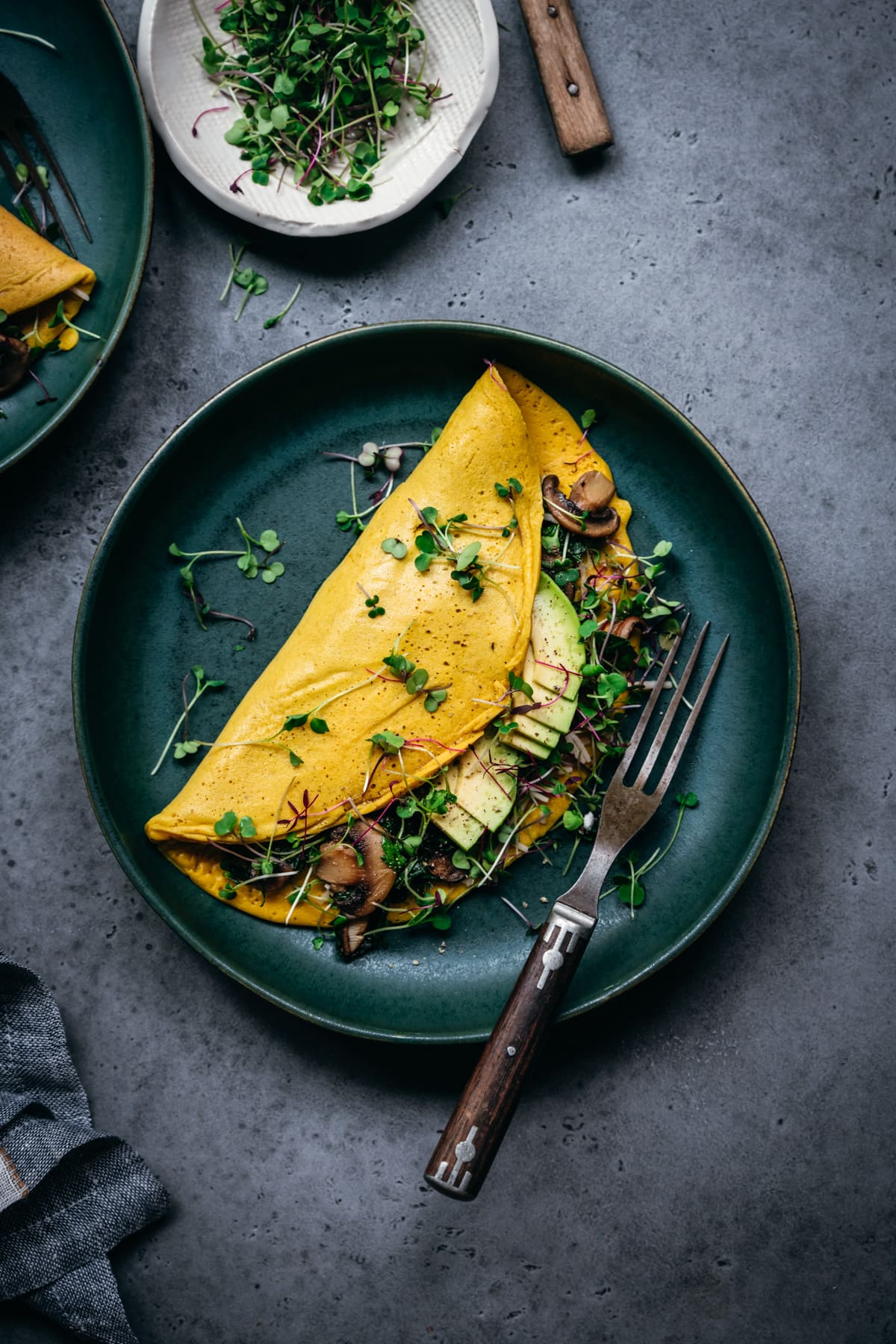 overhead view of vegan chickpea flour omelette with mushroom and spinach filling on teal plate.