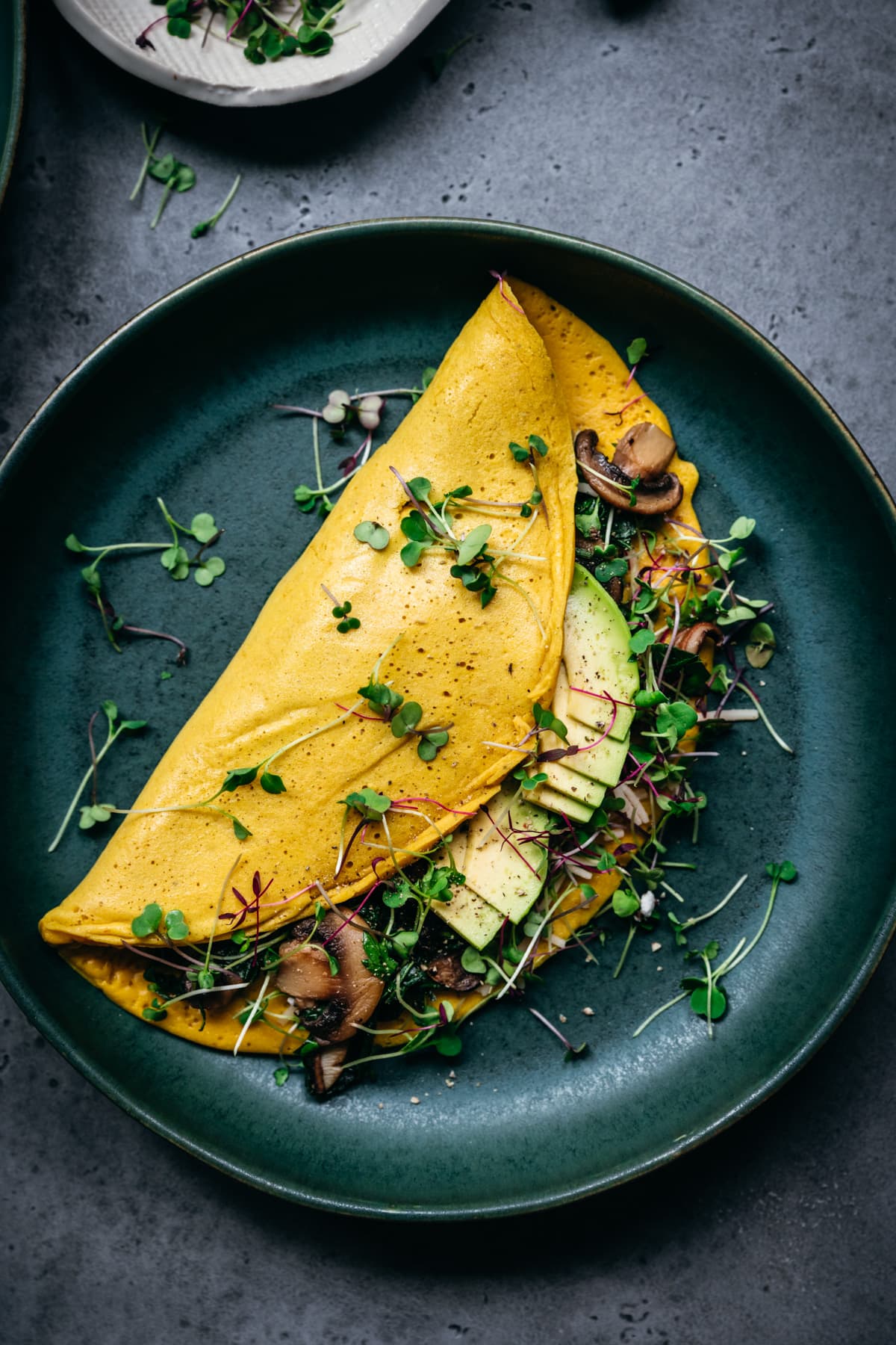 overhead view of vegan chickpea flour omelette with mushroom and spinach filling on teal plate.