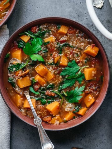 overhead view of quinoa vegetable soup with sweet potatoes in bowl with spoon.