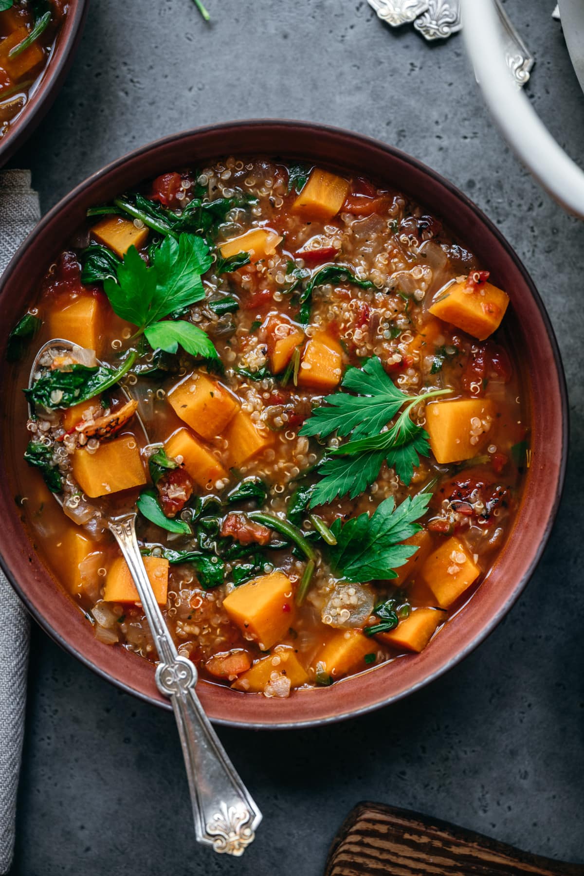 overhead view of quinoa vegetable soup with sweet potatoes in bowl with spoon.