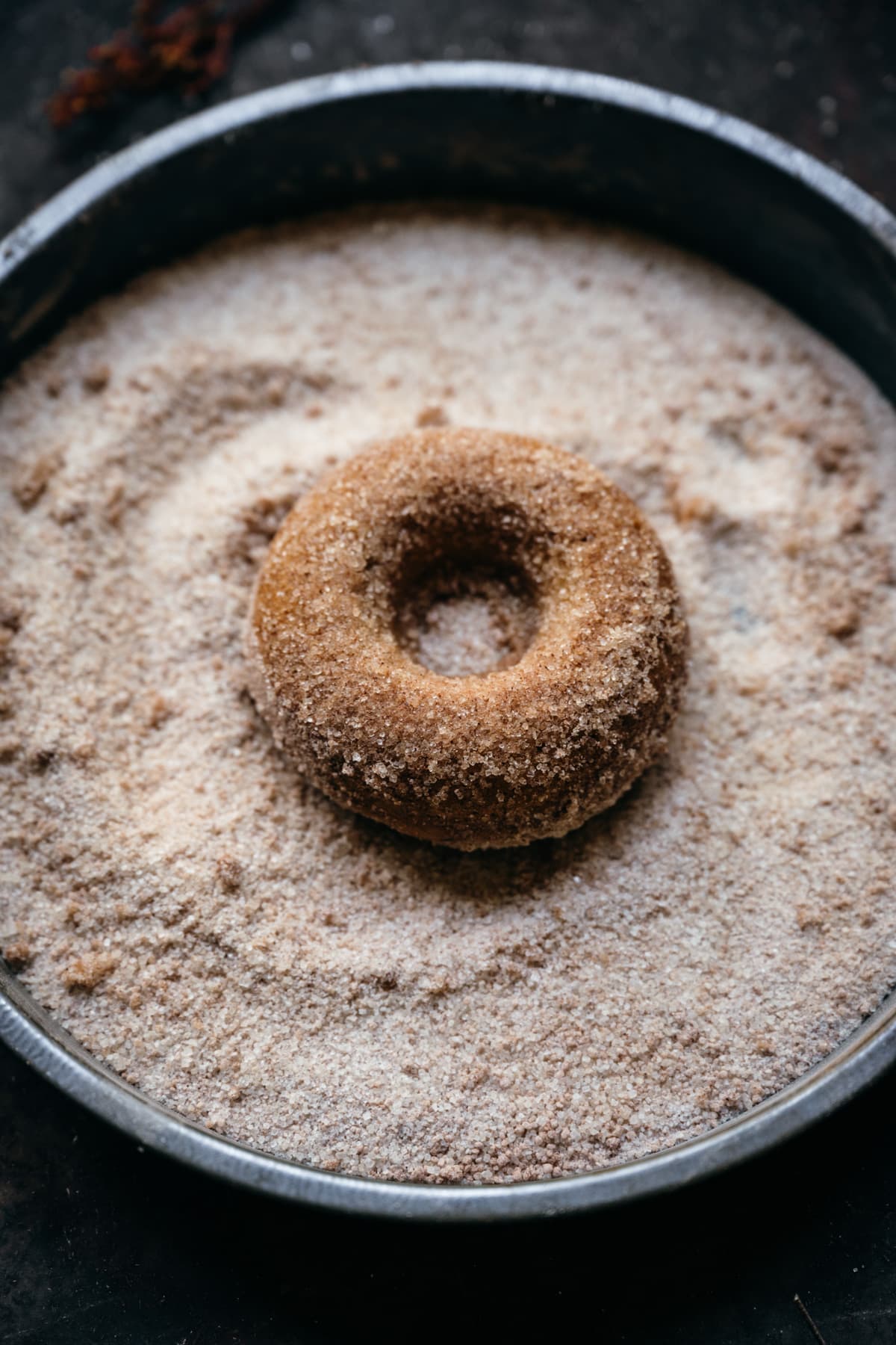 vegan apple cider donut in pan with cinnamon sugar.