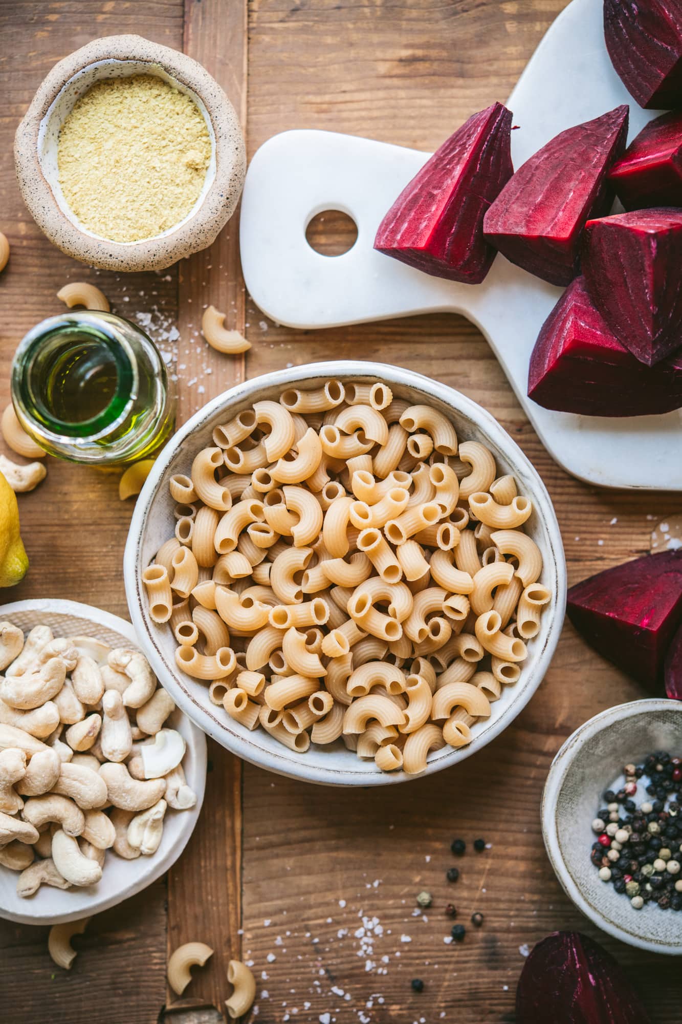 overhead view of ingredients for beet pasta, including uncooked pasta, olive oil, cashews, and beets.