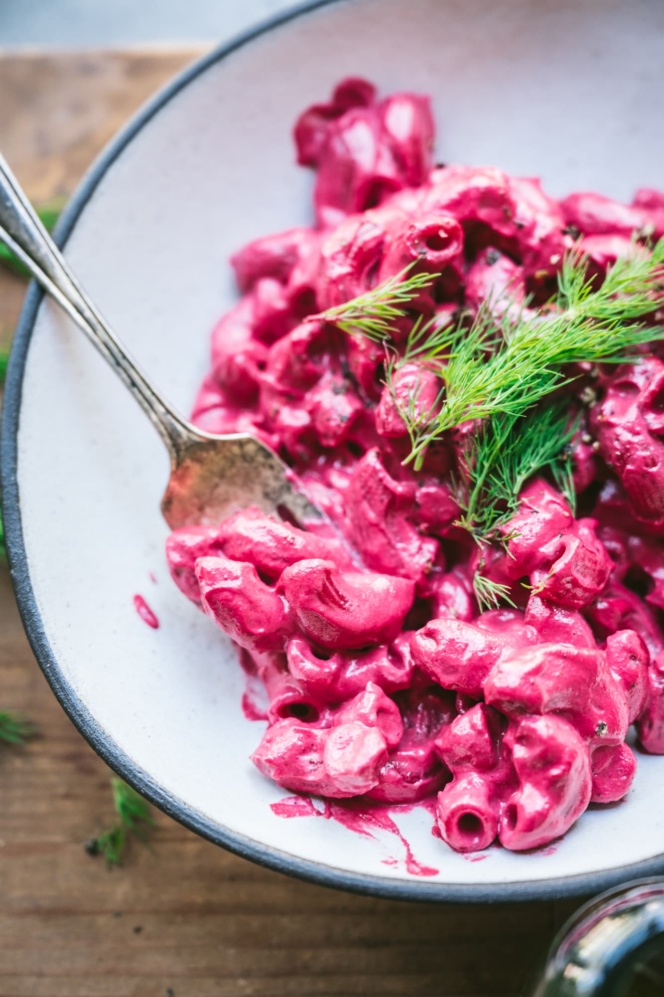 close up side view of creamy vegan beet mac and cheese on a fork in white bowl.