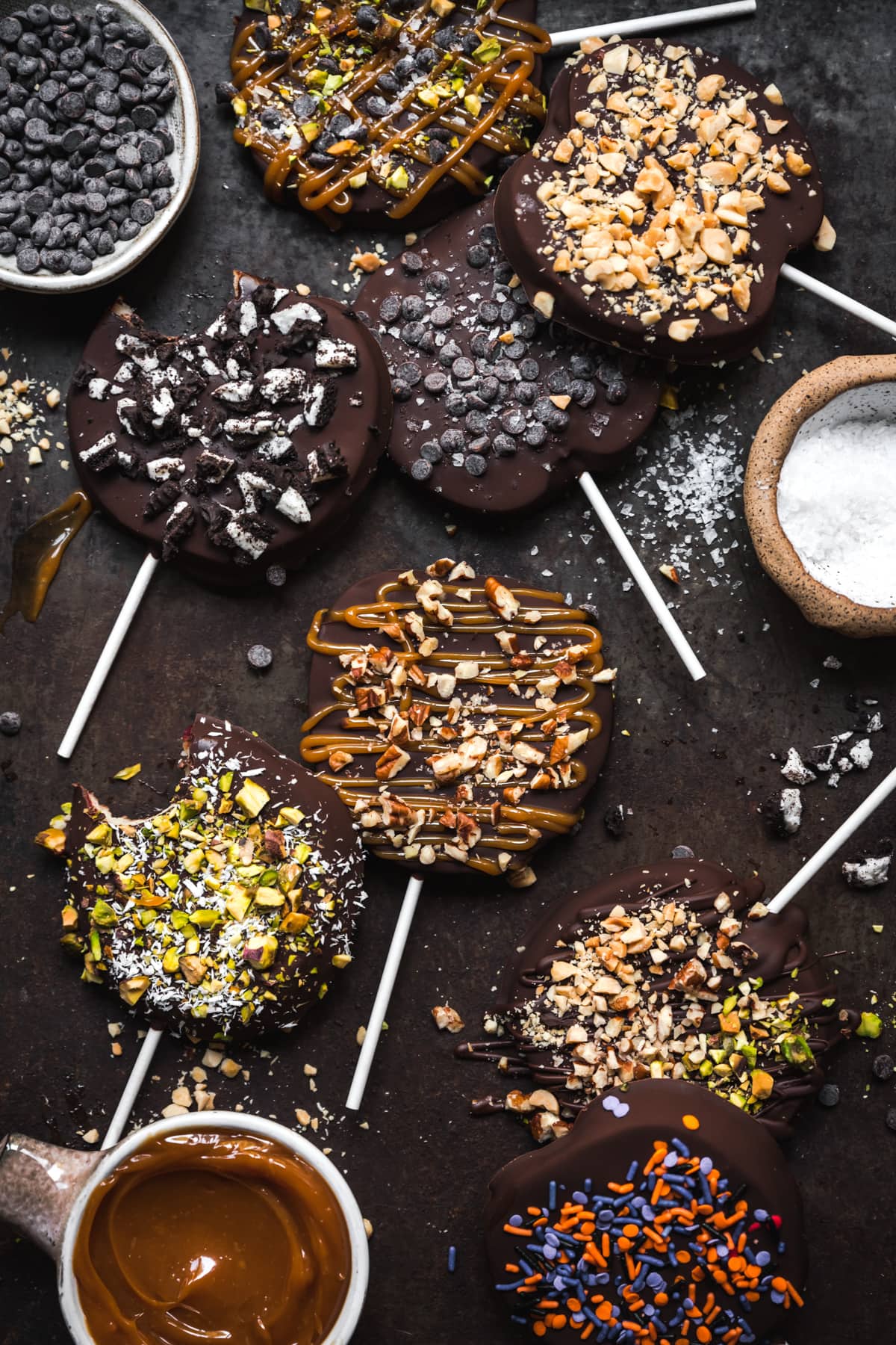 overhead view of chocolate covered apple slices with various toppings on rustic sheet pan.