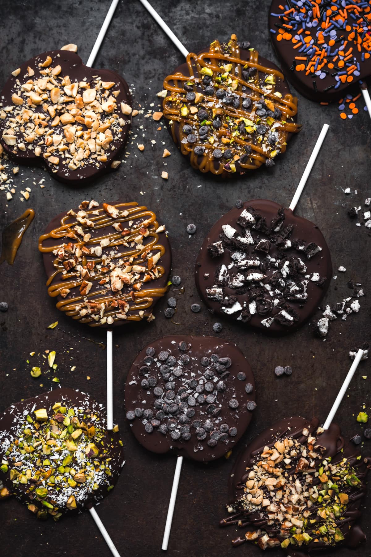 overhead view of chocolate covered apple slices with various toppings on rustic sheet pan.