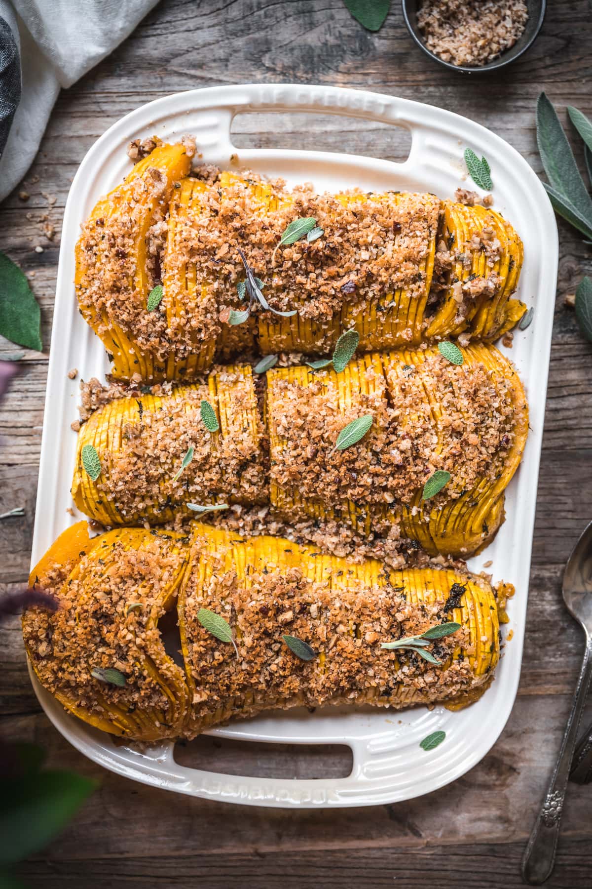 overhead view of hasselback butternut squash on a white platter topped with breadcrumbs.