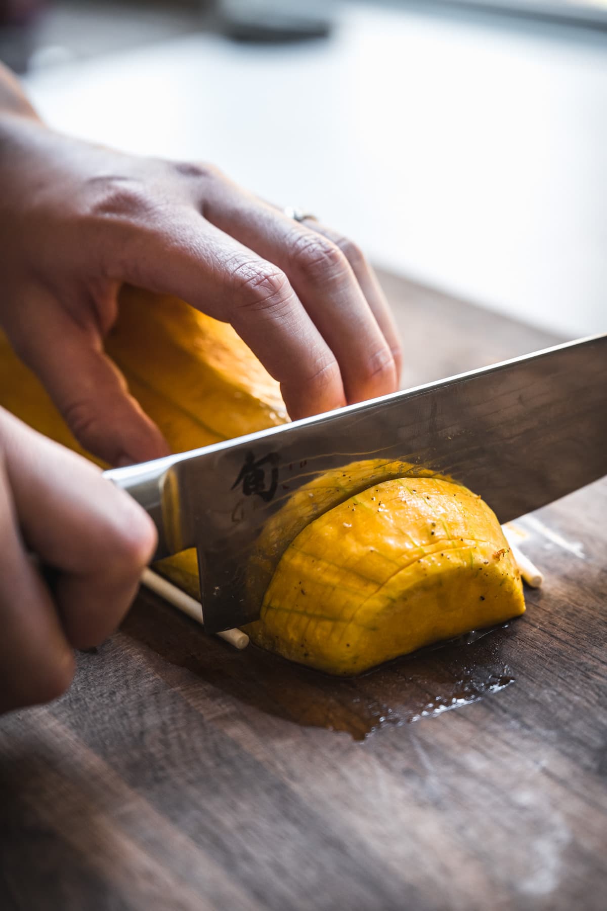 person slicing into a butternut squash with a large knife on a cutting board.