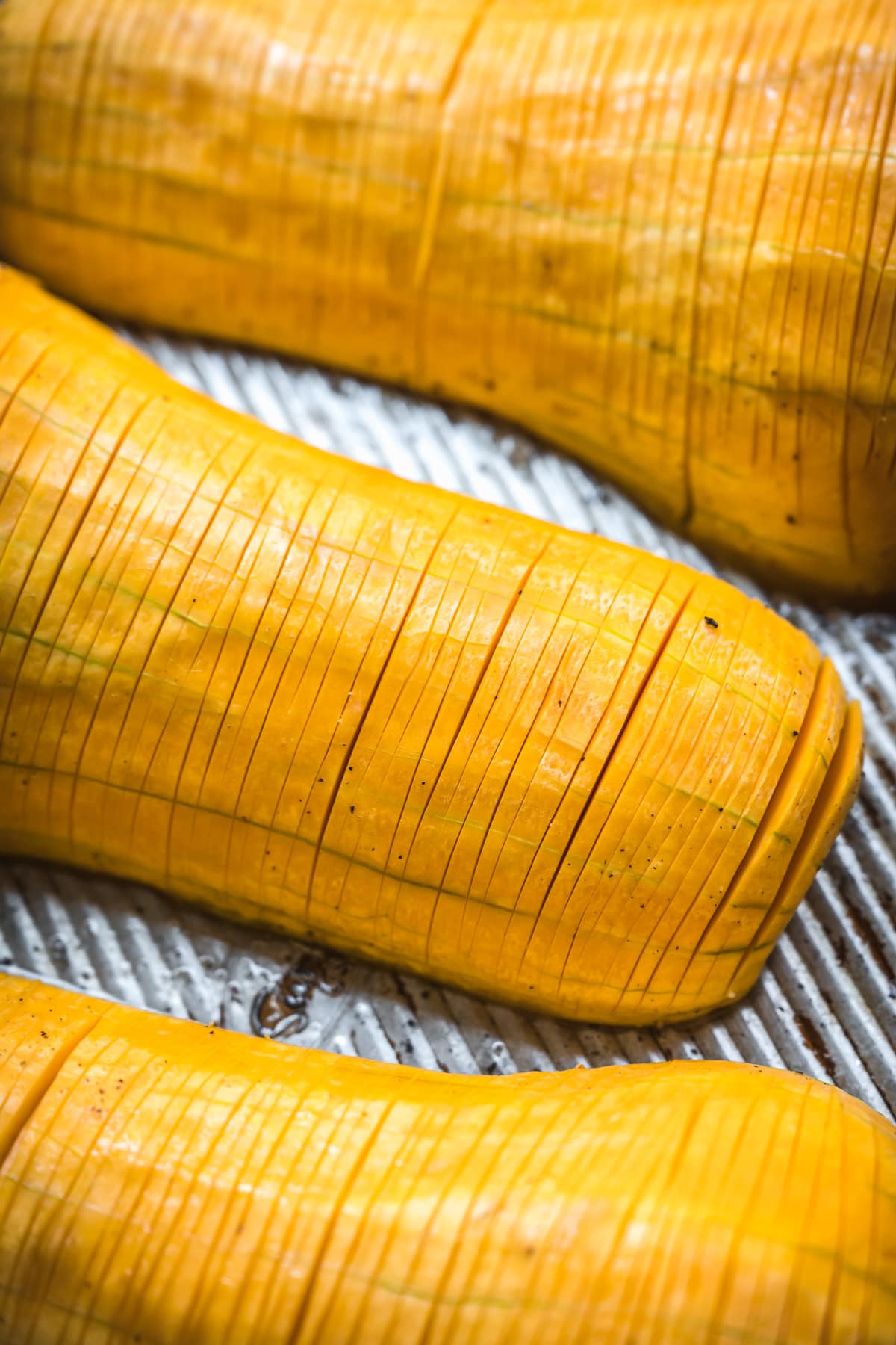 close up view of a butternut squash with hasselback knife cuts on a sheet pan.