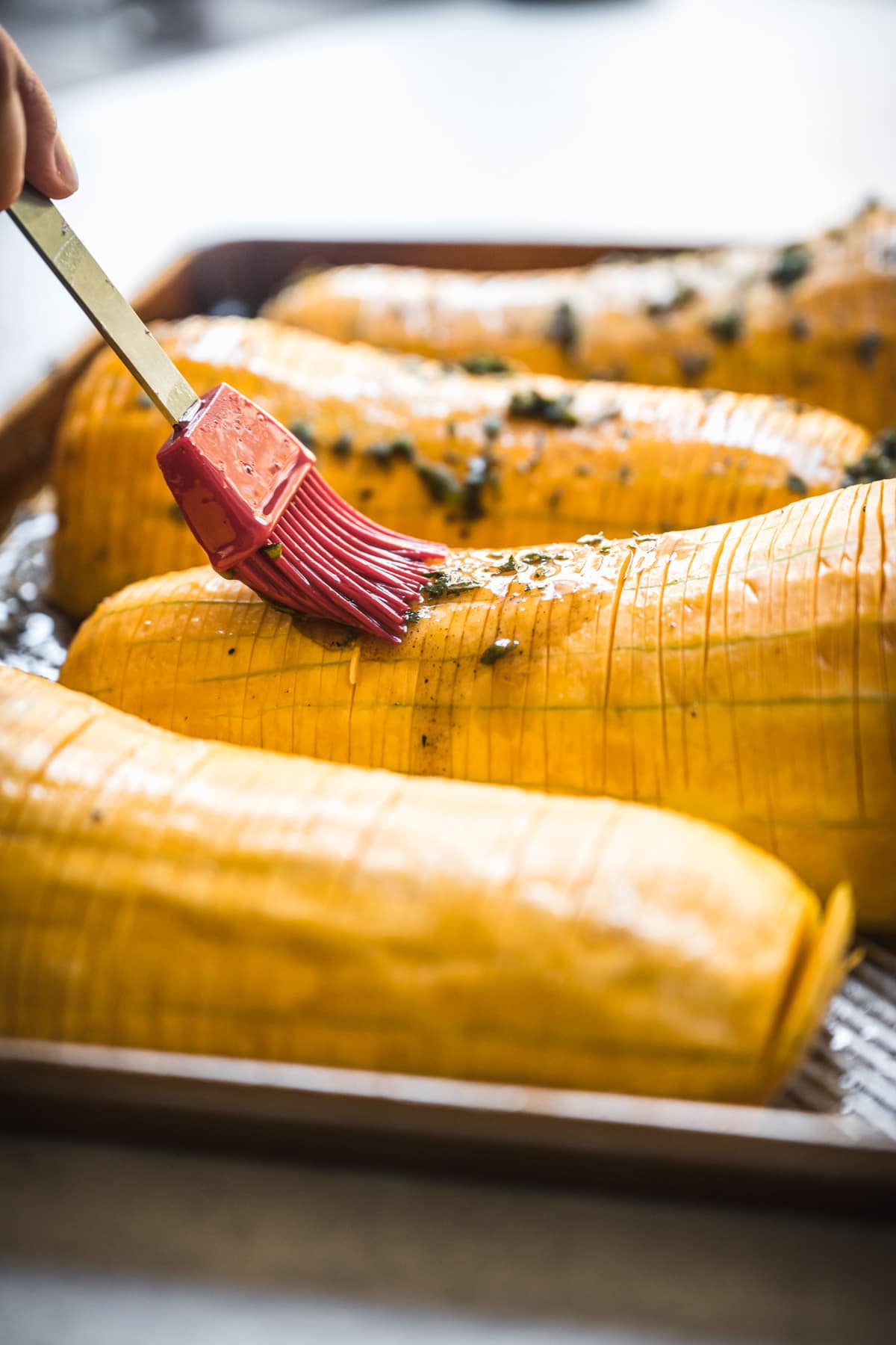 person brushing maple herb butter on hasselback butternut squash.