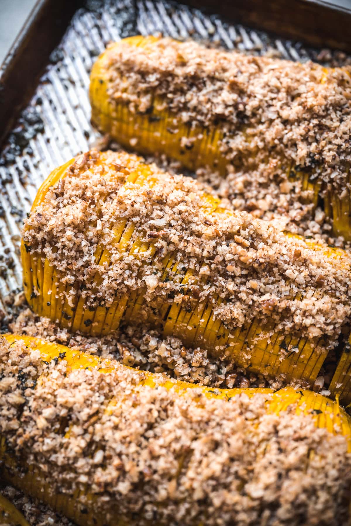 close up view of hasselback butternut squash with breadcrumbs on a sheet pan.