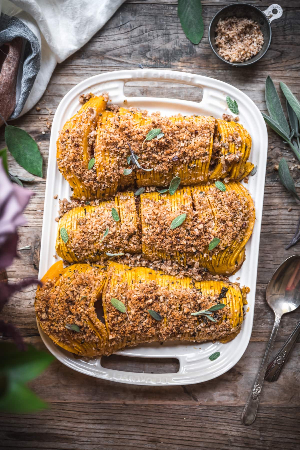 overhead view of hasselback butternut squash on a white platter topped with breadcrumbs.
