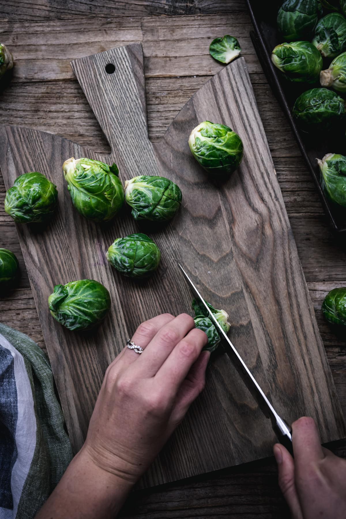 overhead view of a person slicing the stem off of a brussels sprout on a wood cutting board.