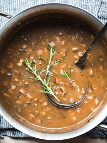 close up overhead view of vegan mushroom gravy in a pot garnished with fresh rosemary.