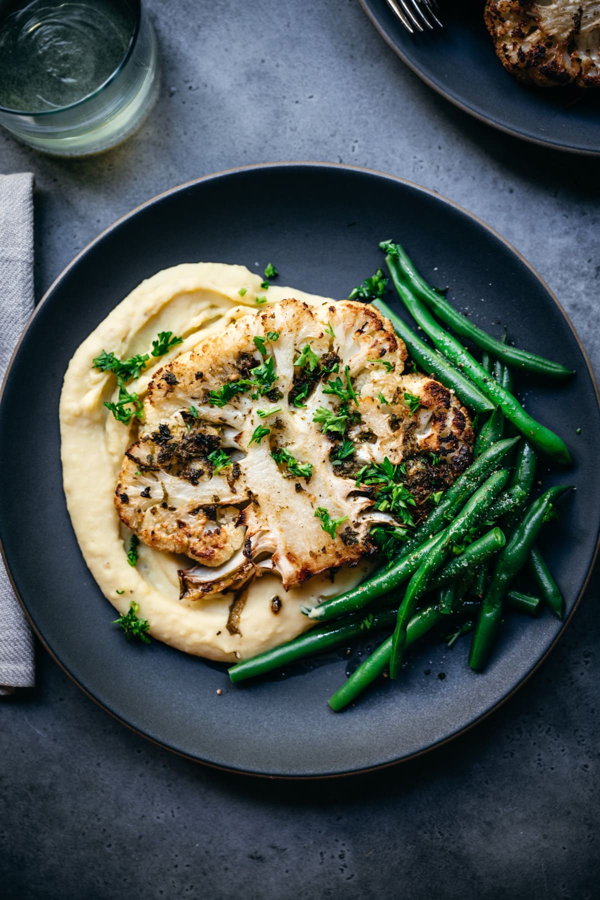 overhead view of roasted cauliflower steak on a plate with mashed potatoes and green beans. 