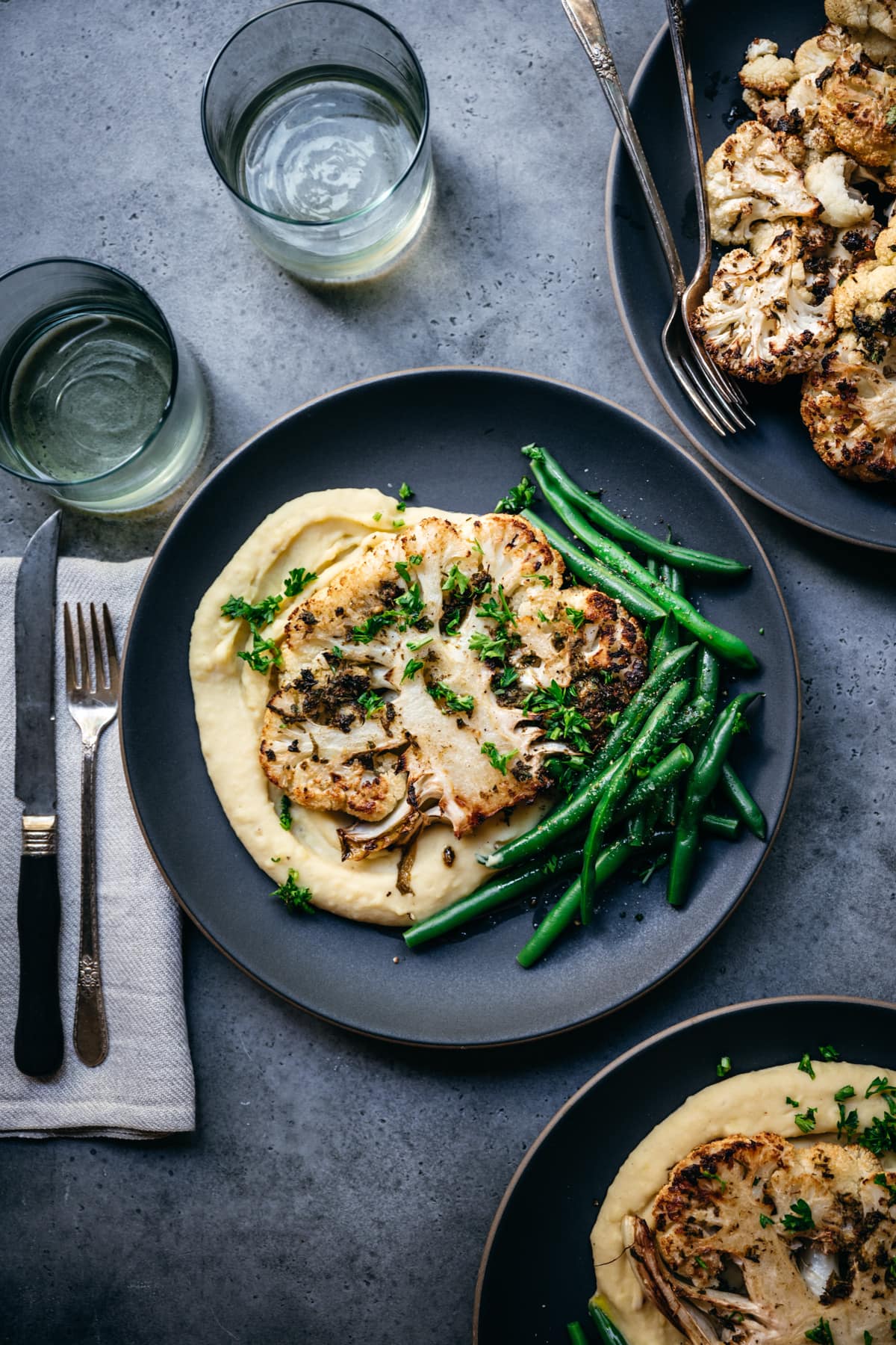 overhead view of roasted cauliflower steak on a plate with mashed potatoes and green beans. 