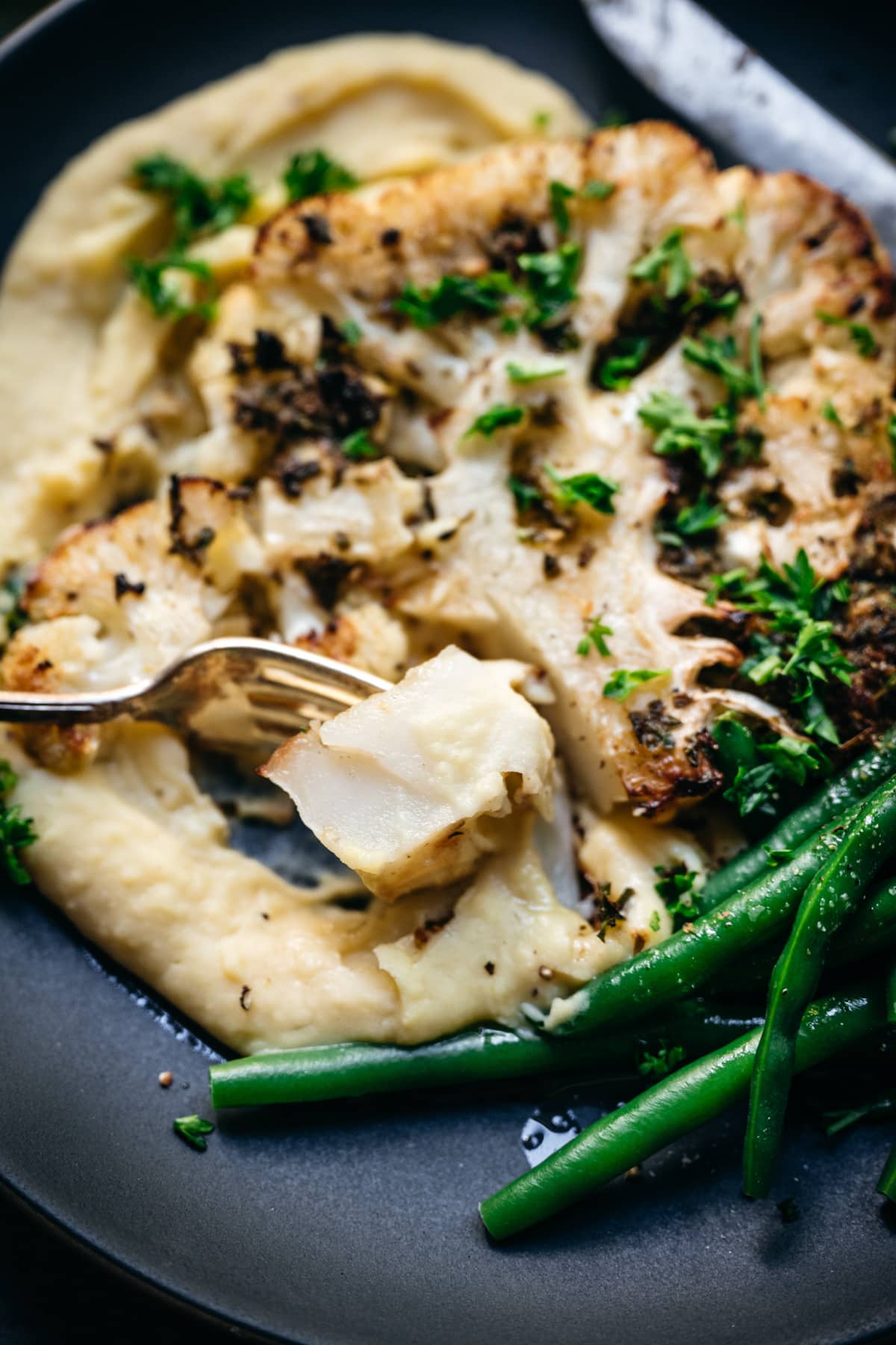 close up view of cauliflower steak piece on fork. 