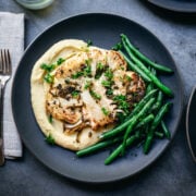 overhead view of roasted cauliflower steak on a plate with mashed potatoes and green beans.