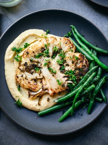 overhead view of roasted cauliflower steak on a plate with mashed potatoes and green beans.