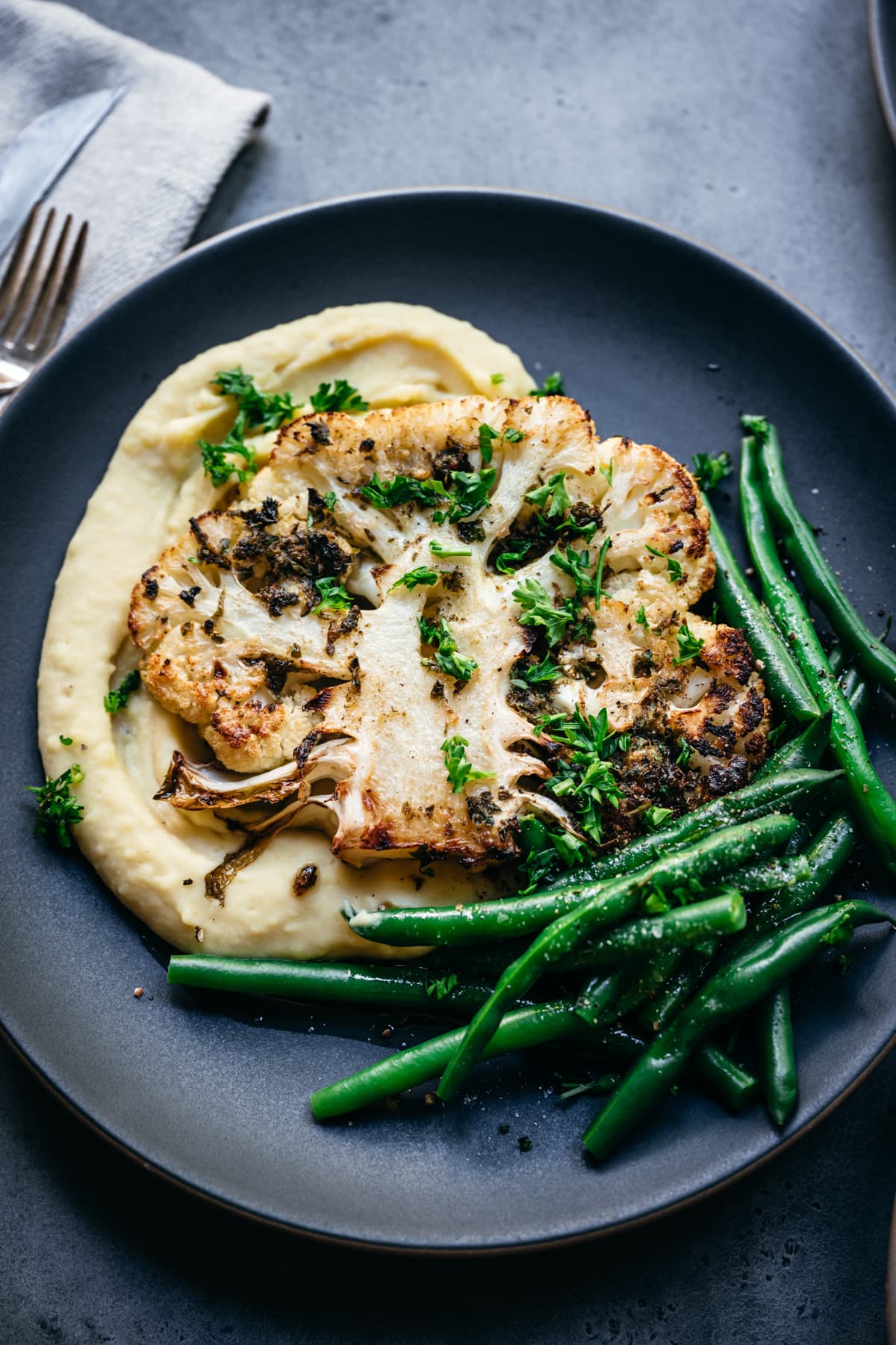 overhead view of roasted cauliflower steak on a plate with mashed potatoes and green beans. 