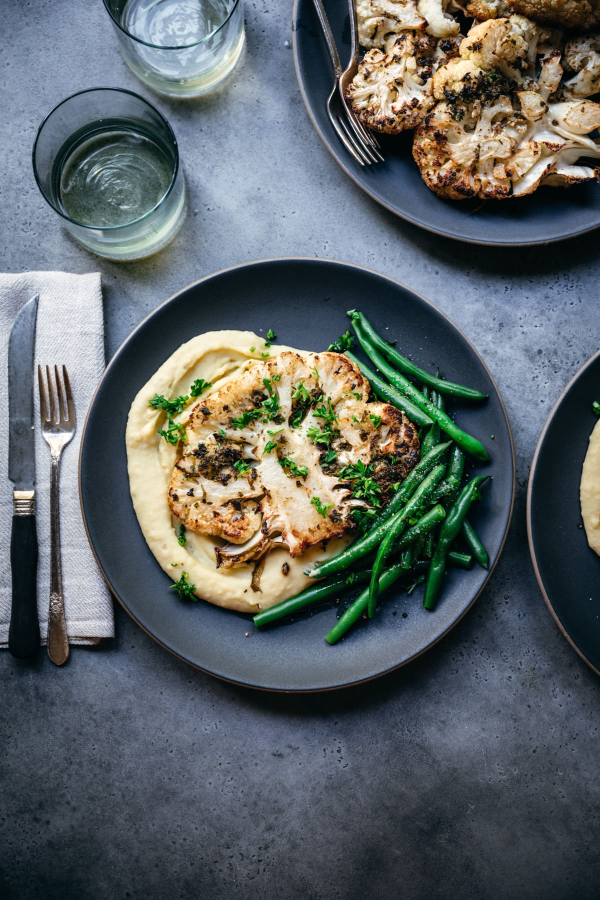 overhead view of roasted cauliflower steak on a plate with mashed potatoes and green beans. 