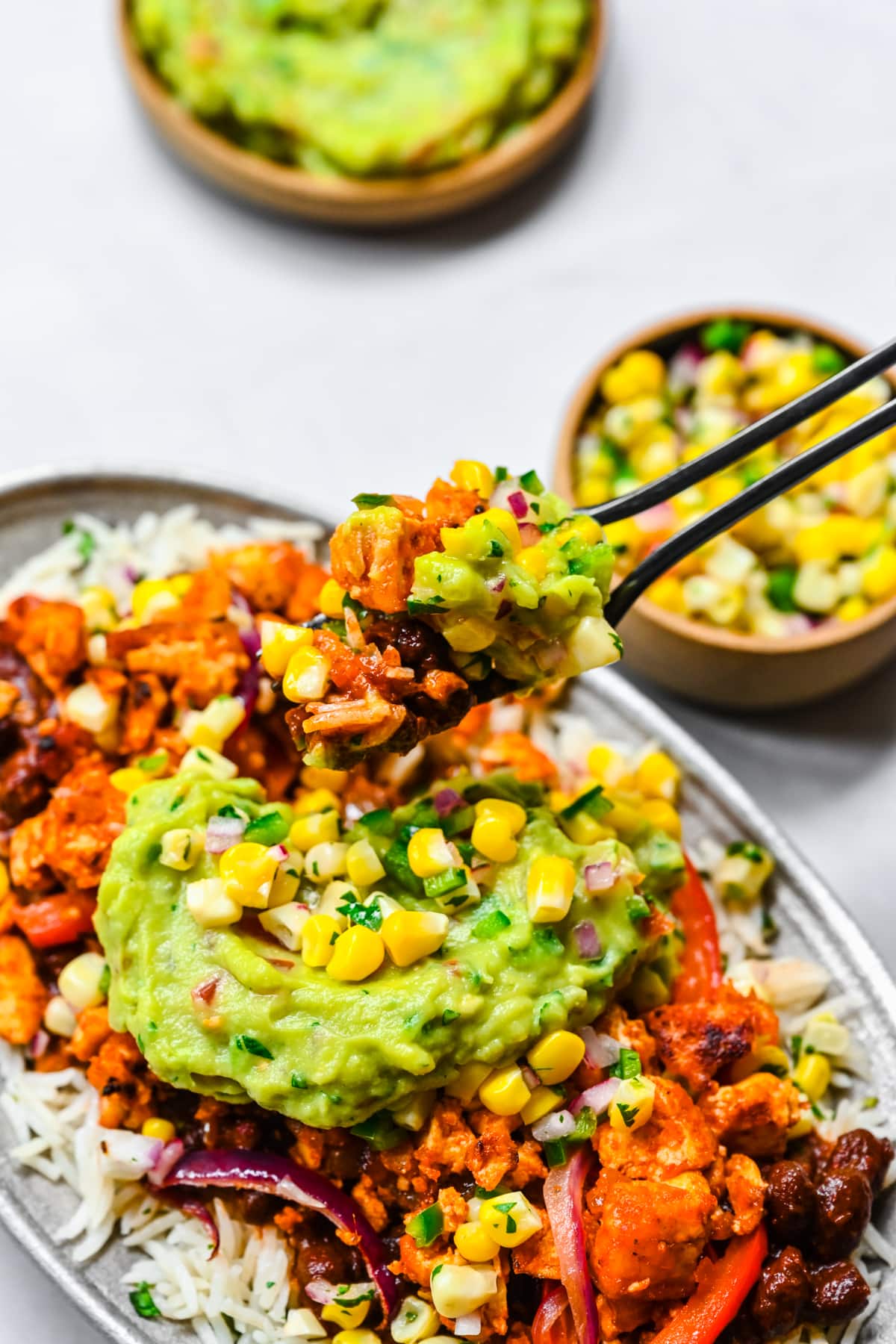 Close up side view of sofritas tofu in a burrito bowl with guacamole and corn salsa.