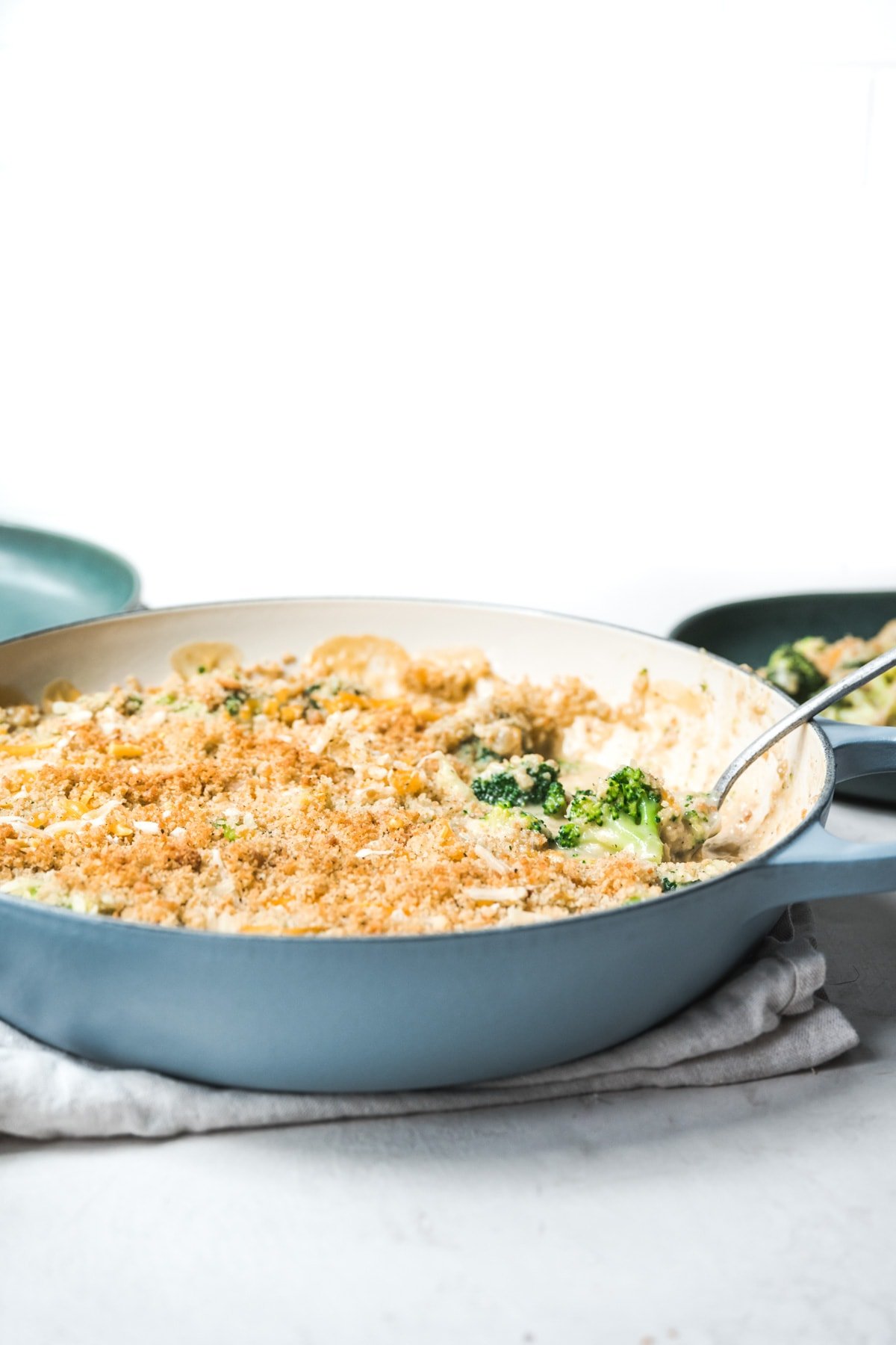 side view of large skillet with vegan broccoli casserole and serving spoon.