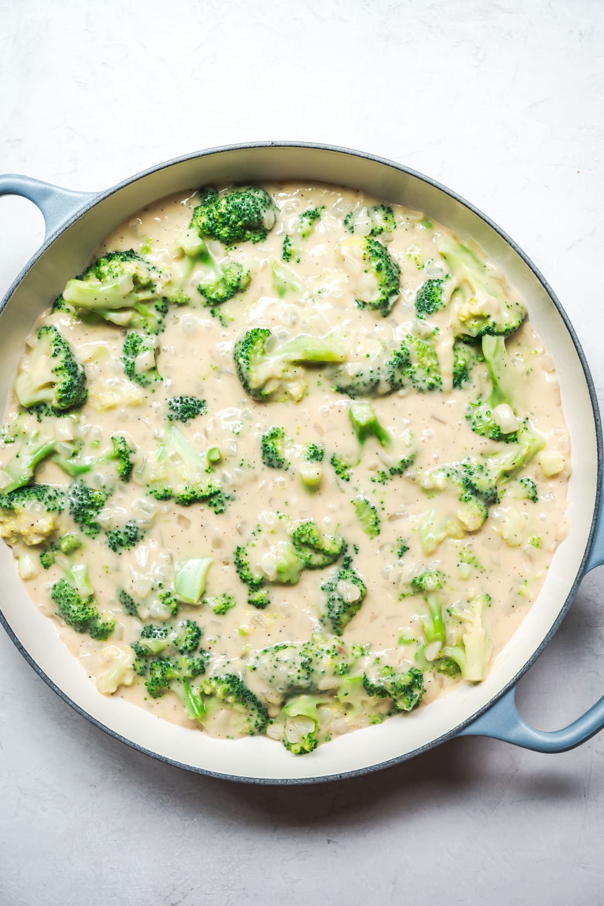 overhead view of cheesy vegan broccoli casserole in large skillet before baking.