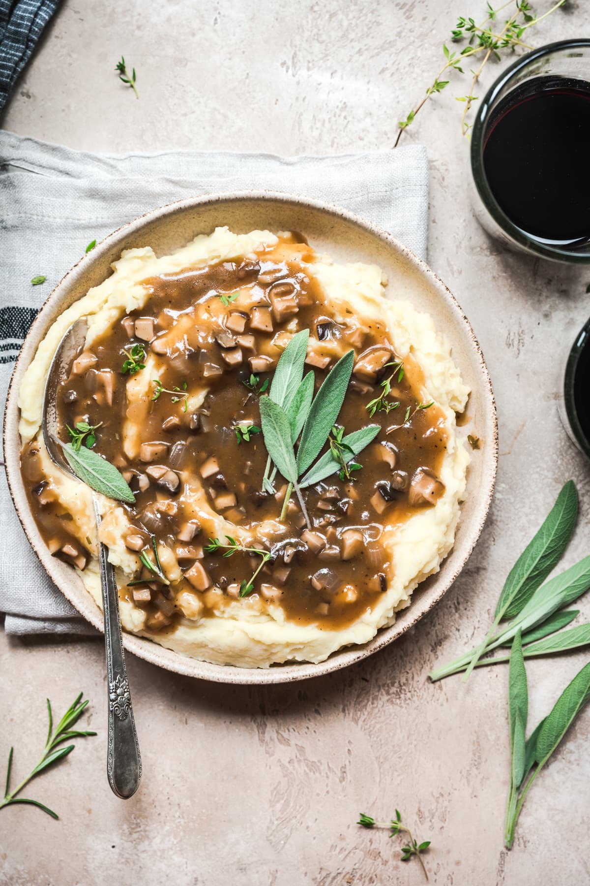 overhead view of bowl of mashed potatoes topped with vegan mushroom gravy and fresh sage.