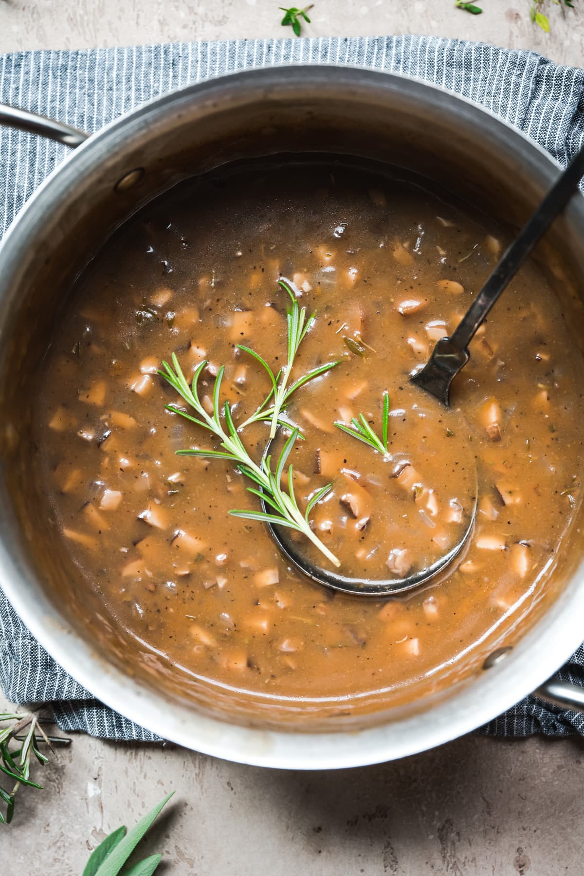 close up overhead view of vegan mushroom gravy in a pot garnished with fresh rosemary.