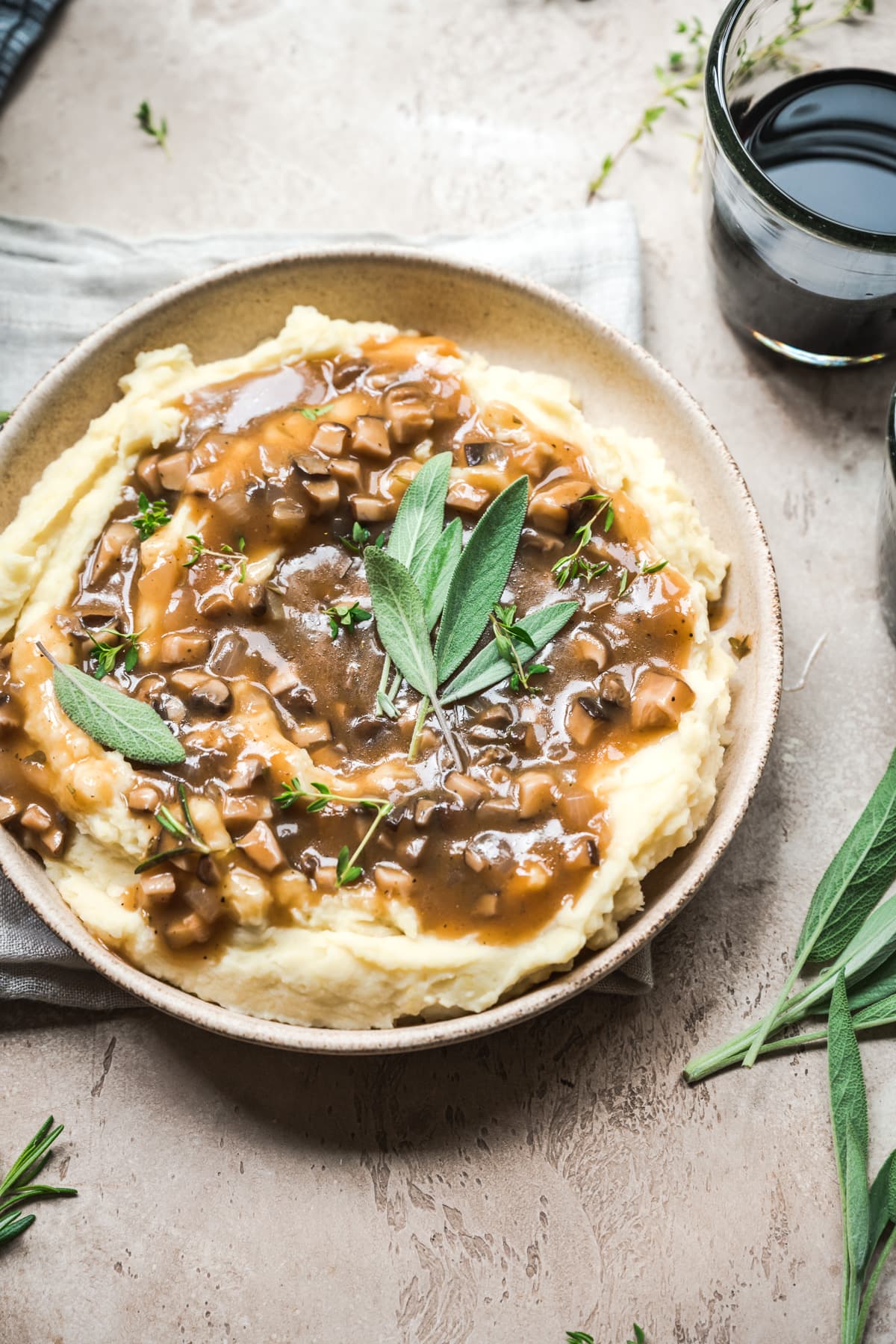 close up view of bowl of mashed potatoes topped with vegan mushroom gravy and fresh sage.