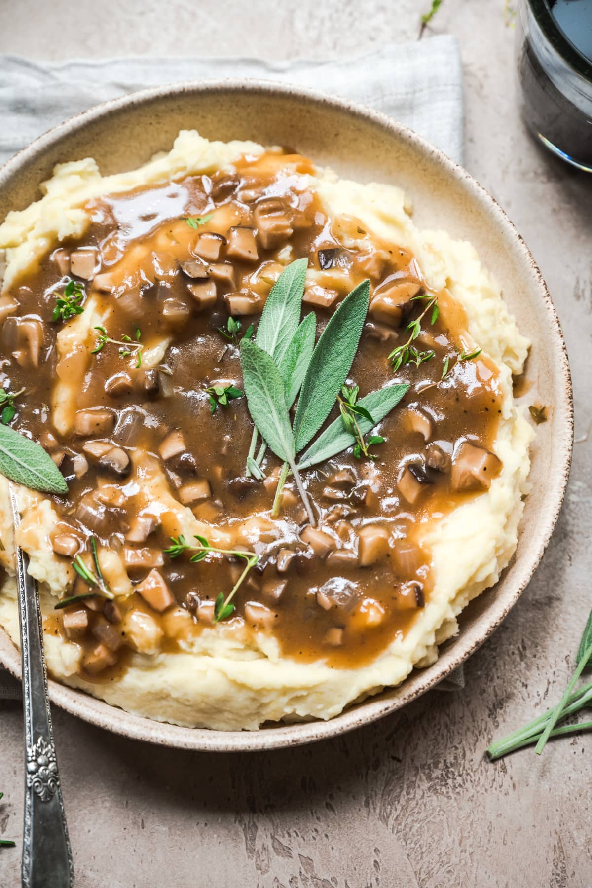 close up view of bowl of mashed potatoes topped with vegan mushroom gravy and fresh sage.