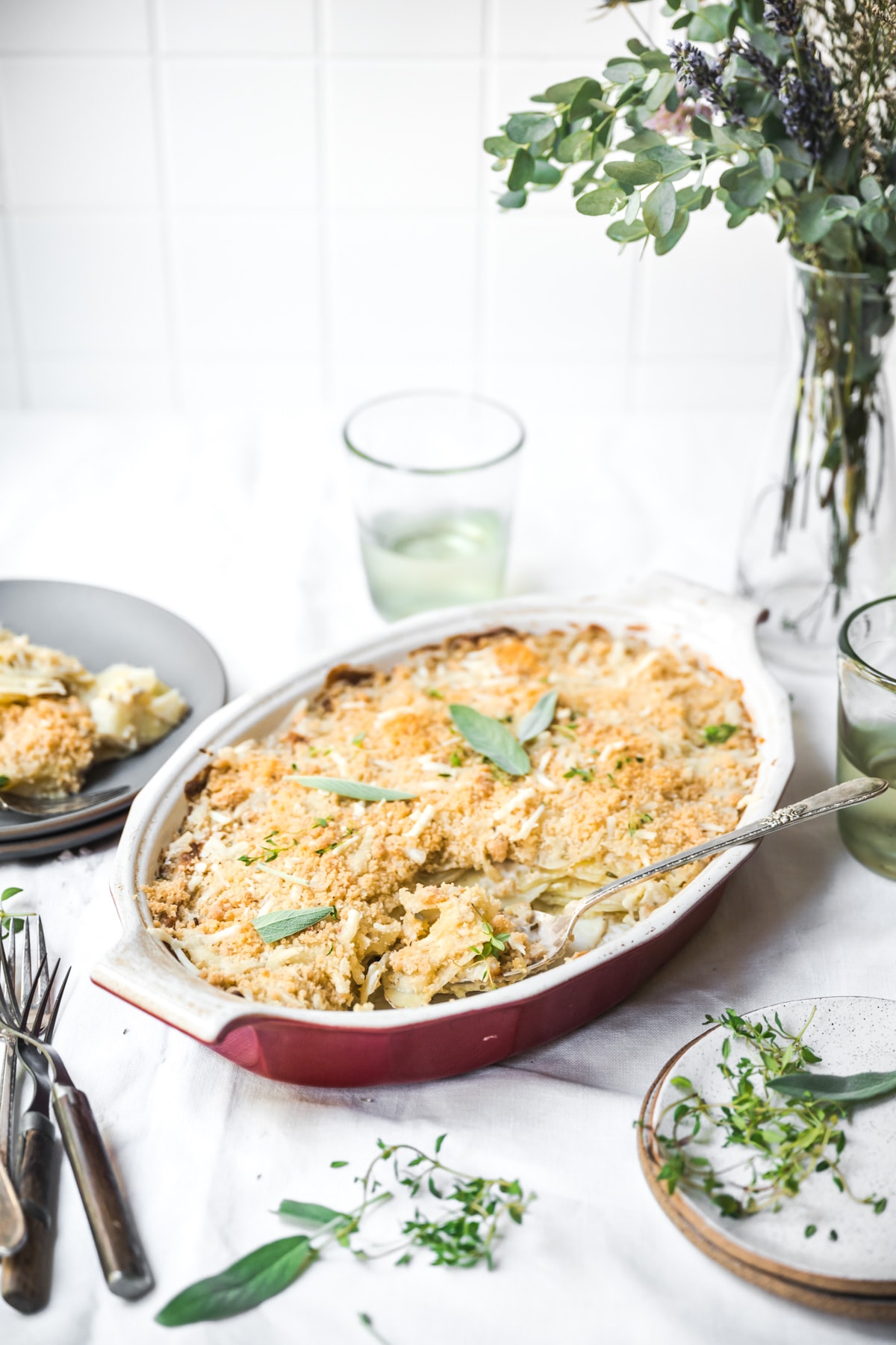 side view of vegan scalloped potatoes with breadcrumb topping in a casserole dish on white linen tablecloth.