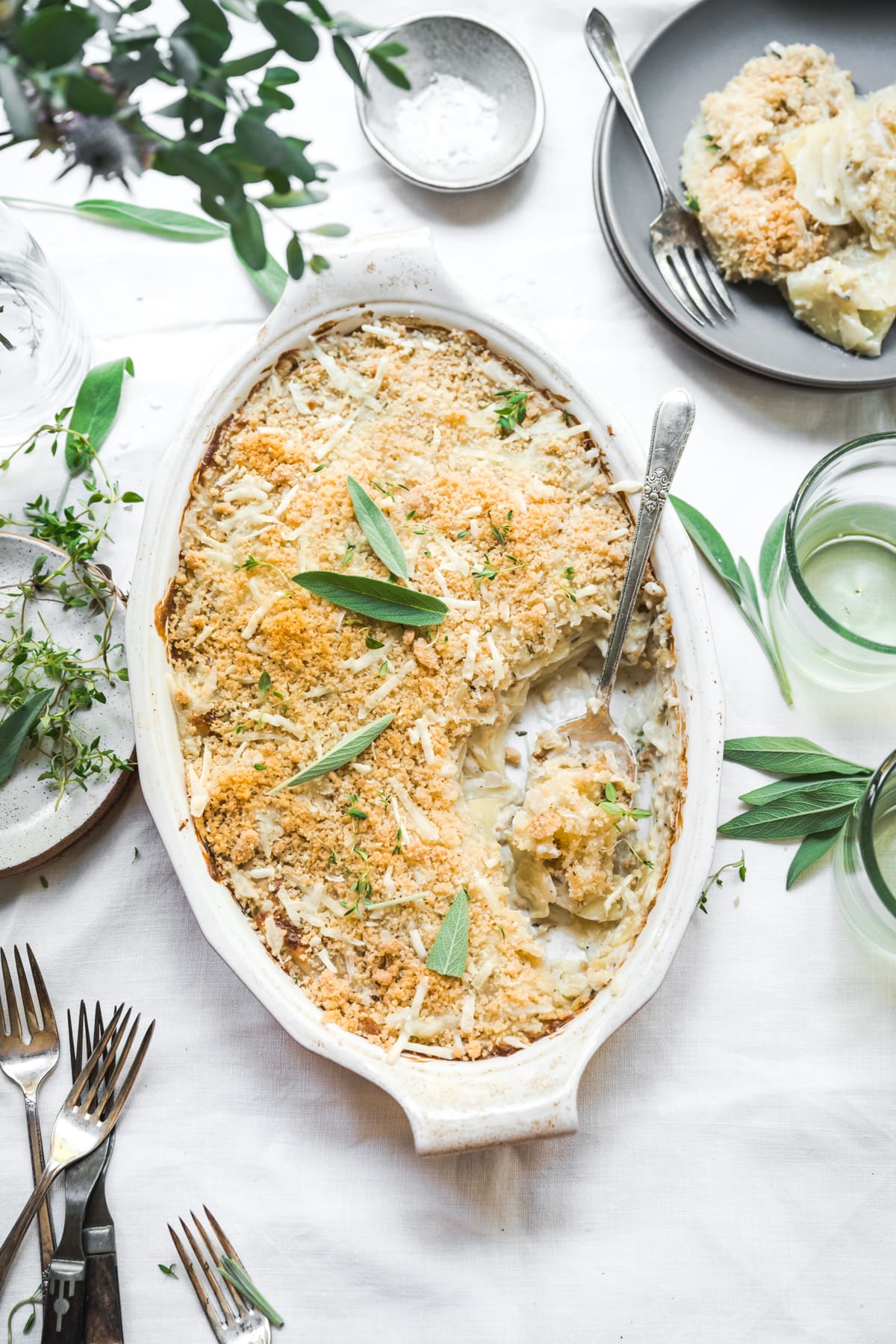 overhead view of vegan scalloped potatoes with breadcrumb topping in a casserole dish on white linen tablecloth.