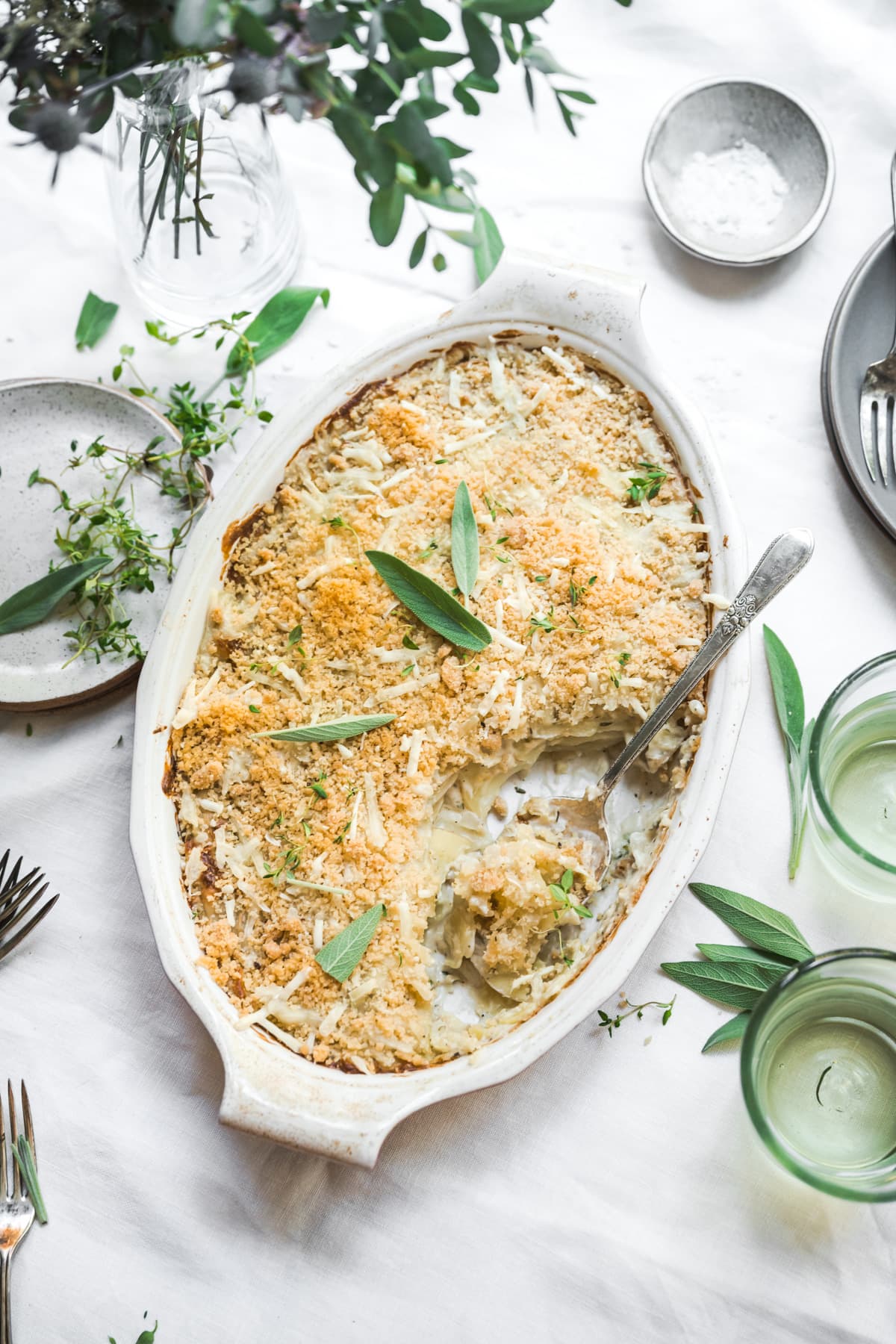 overhead view of vegan scalloped potatoes with breadcrumb topping in a casserole dish on white linen tablecloth.