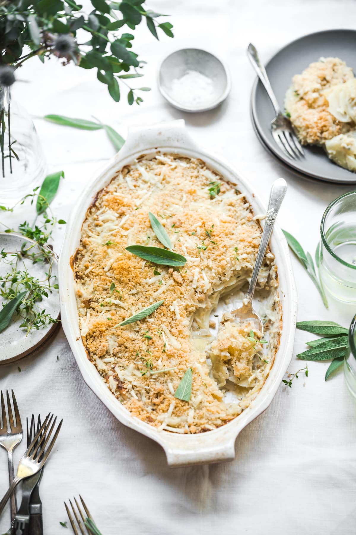 overhead view of vegan scalloped potatoes with breadcrumb topping in a casserole dish on white linen tablecloth.