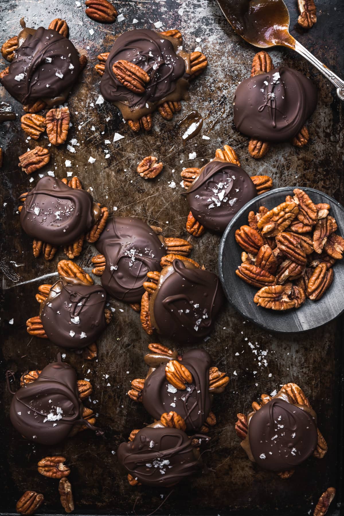 overhead view of vegan chocolate caramel pecan turtles on an antique baking sheet.