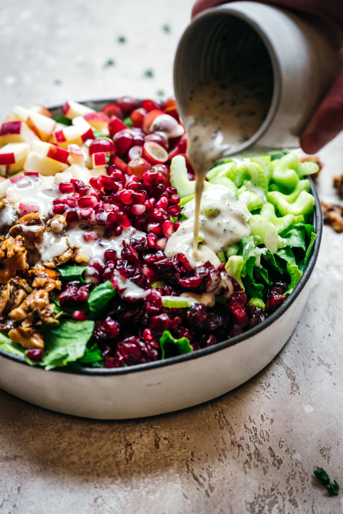 person pouring yogurt dressing onto waldorf salad.